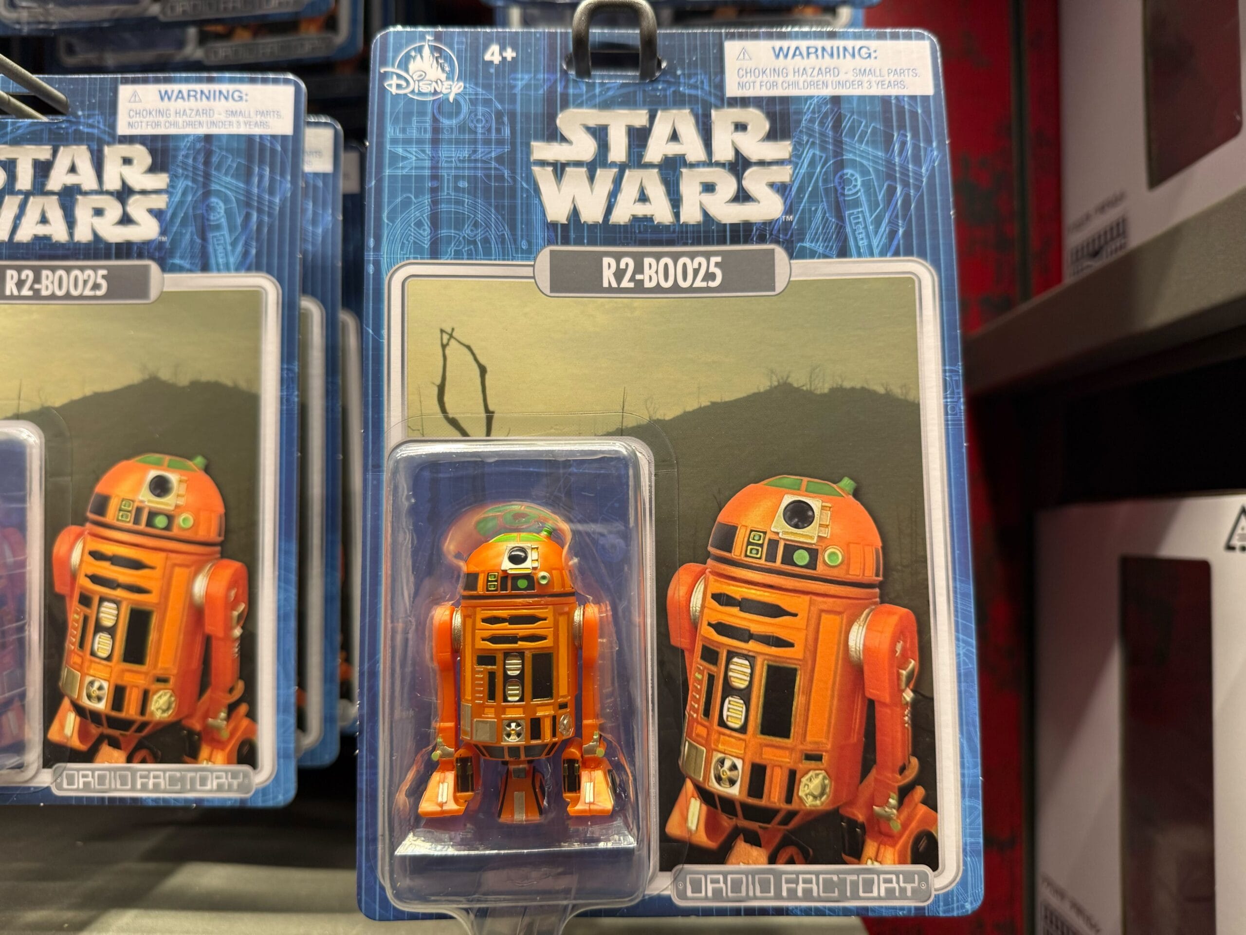 Star Wars R2-B0025 orange droid toy in packaging, displayed on a store shelf under Droid Factory branding.