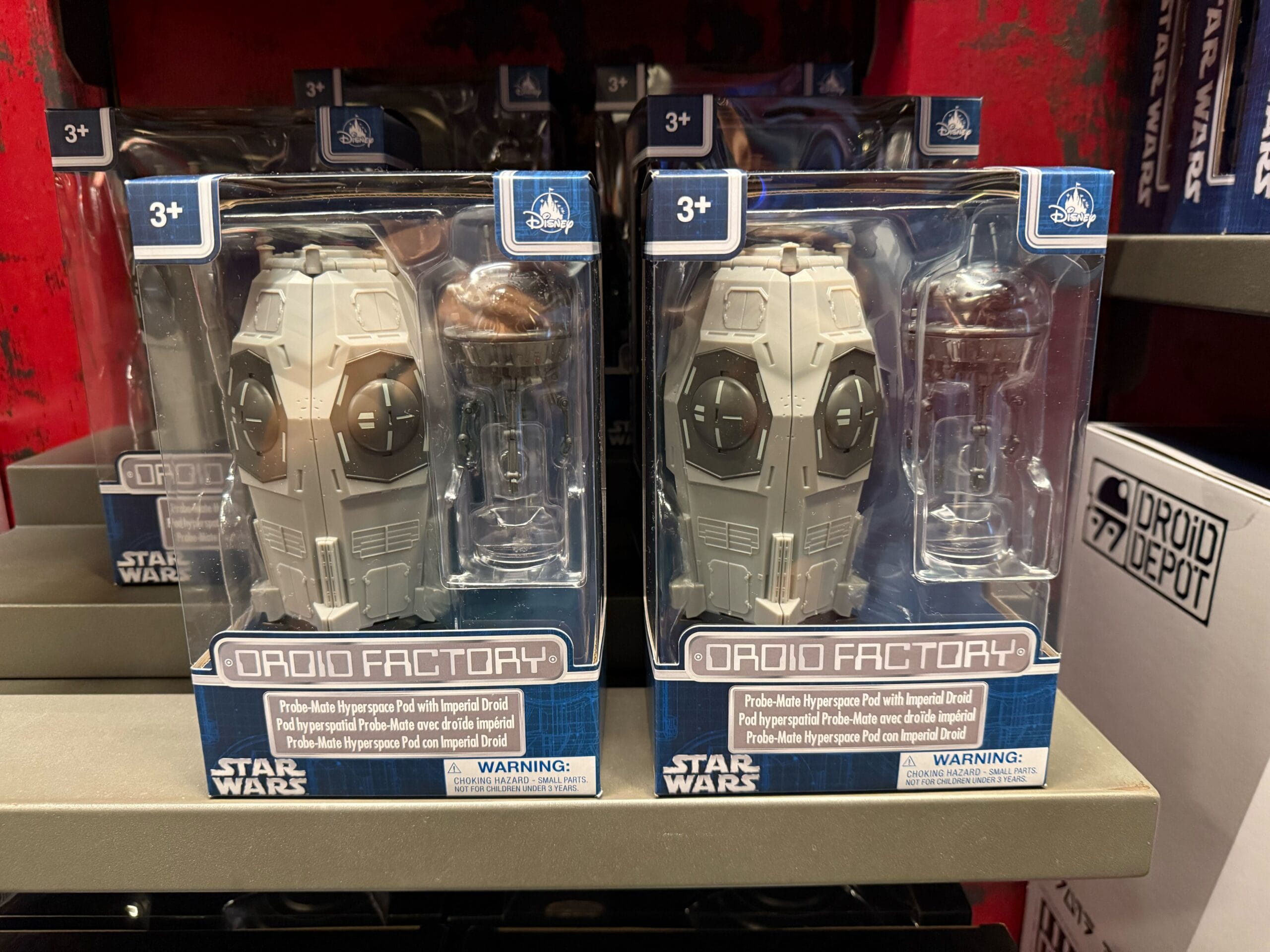 Two Star Wars Droid Factory toy packs on a store shelf, each containing a gray droid and a small silver accessory.