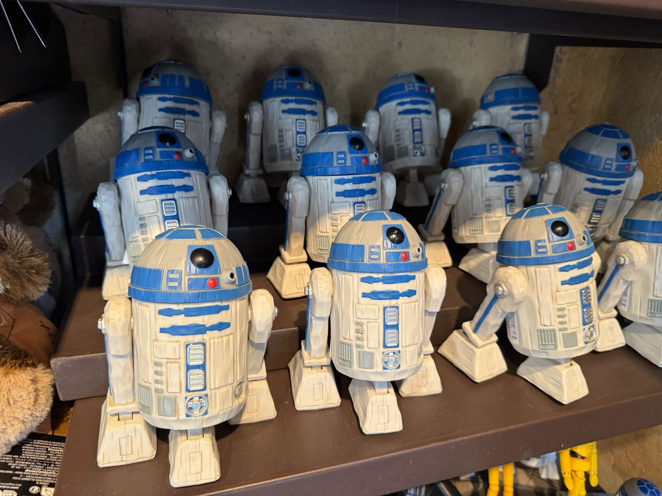 A shelf displays multiple R2-D2 figures in rows, standing side by side in a store setting.