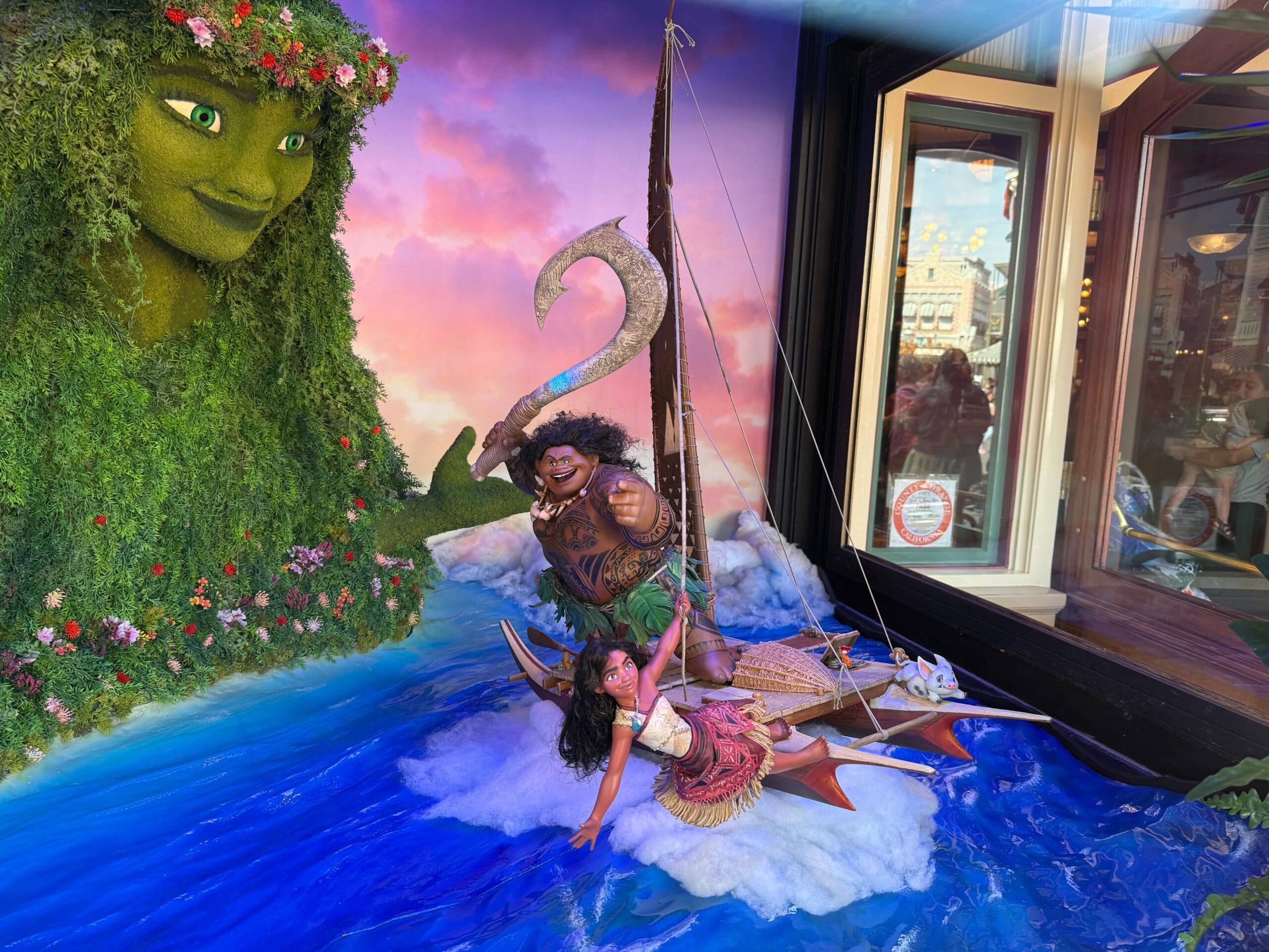 A Moana-themed display features Moana and Maui on a raft, with Te Fiti’s face in greenery, against a colorful sky backdrop.