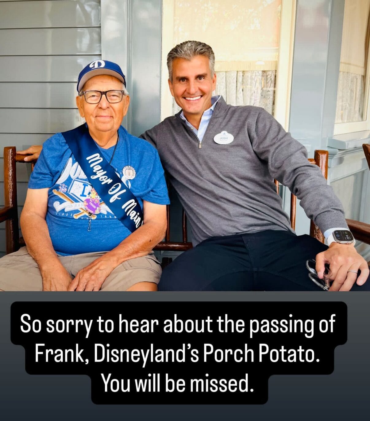 Two men sit together smiling on a porch; one wears a sash reading "Mayor of Main St." and a Disneyland hat.