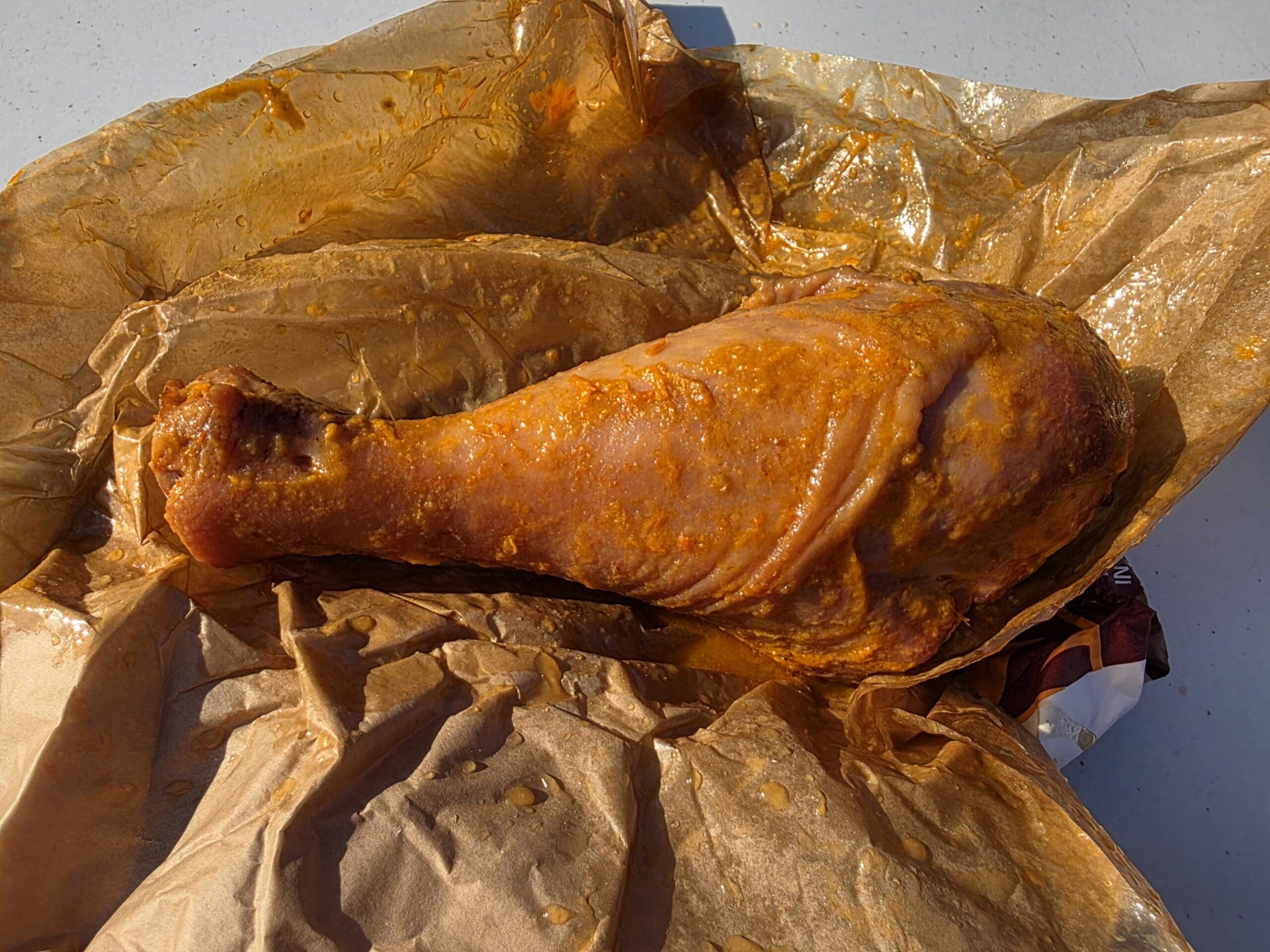 A large, seasoned turkey leg wrapped in greasy brown parchment paper, perfect for ODV Halloween festivities.