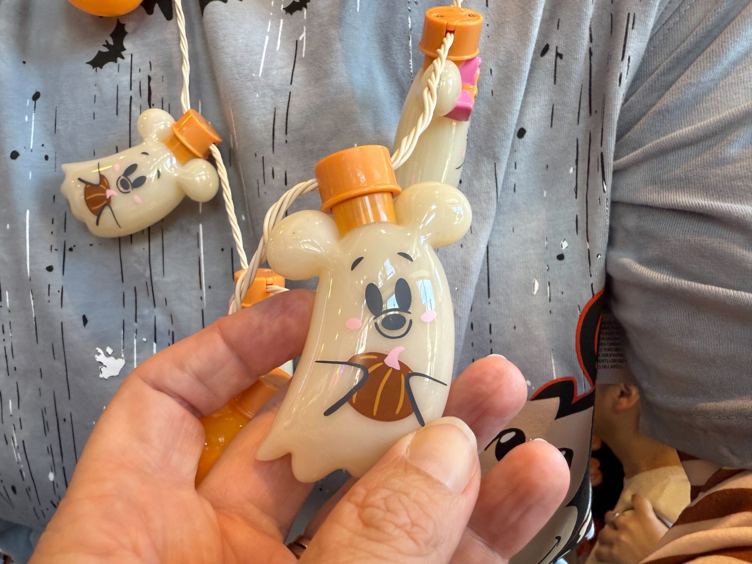 A hand holds a ghost-shaped Halloween merchandise container with matching designs, inspired by Disneyland.