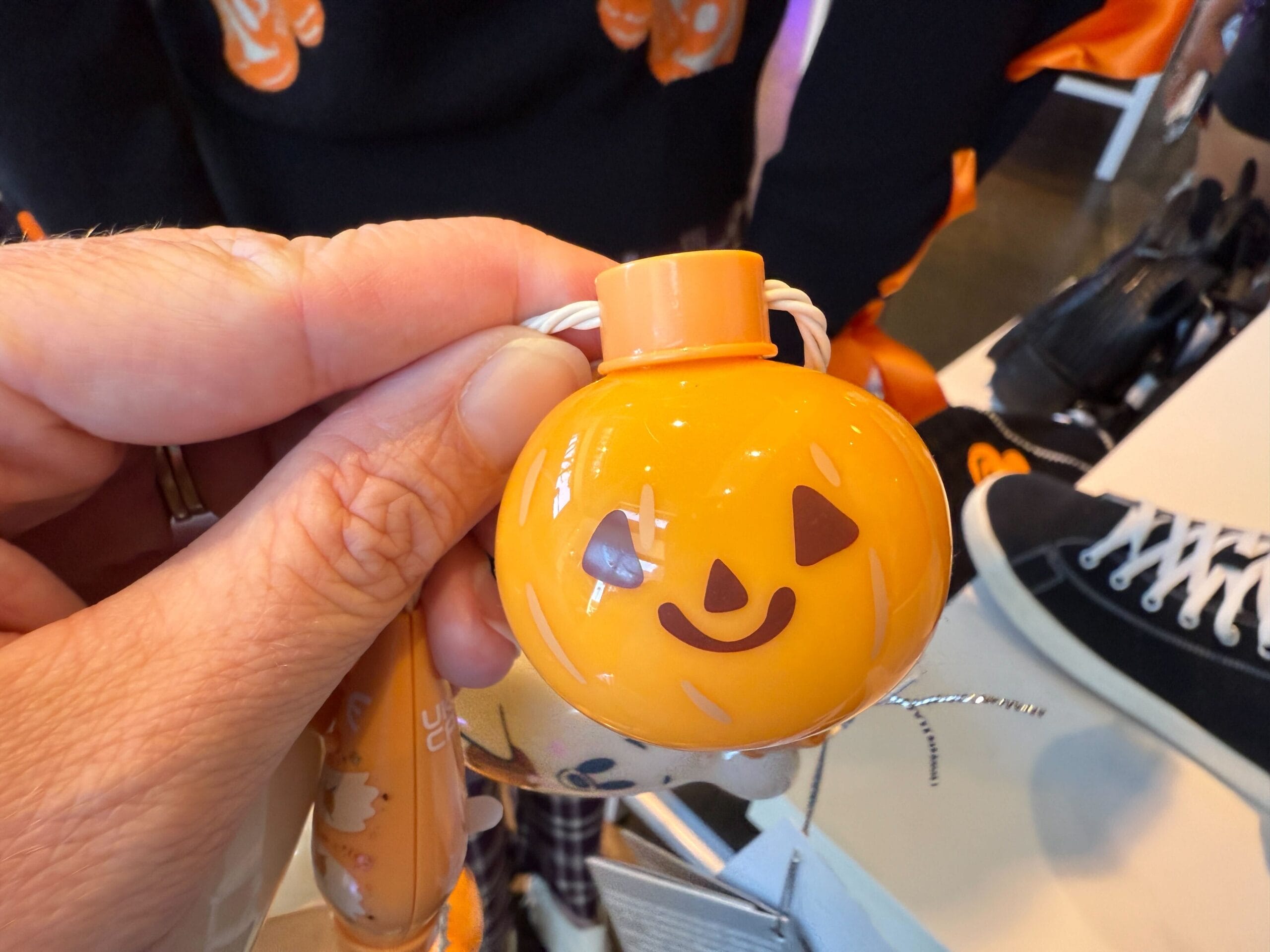 A hand holds a small orange pumpkin ornament from the Disneyland Halloween merchandise collectibles collection.
