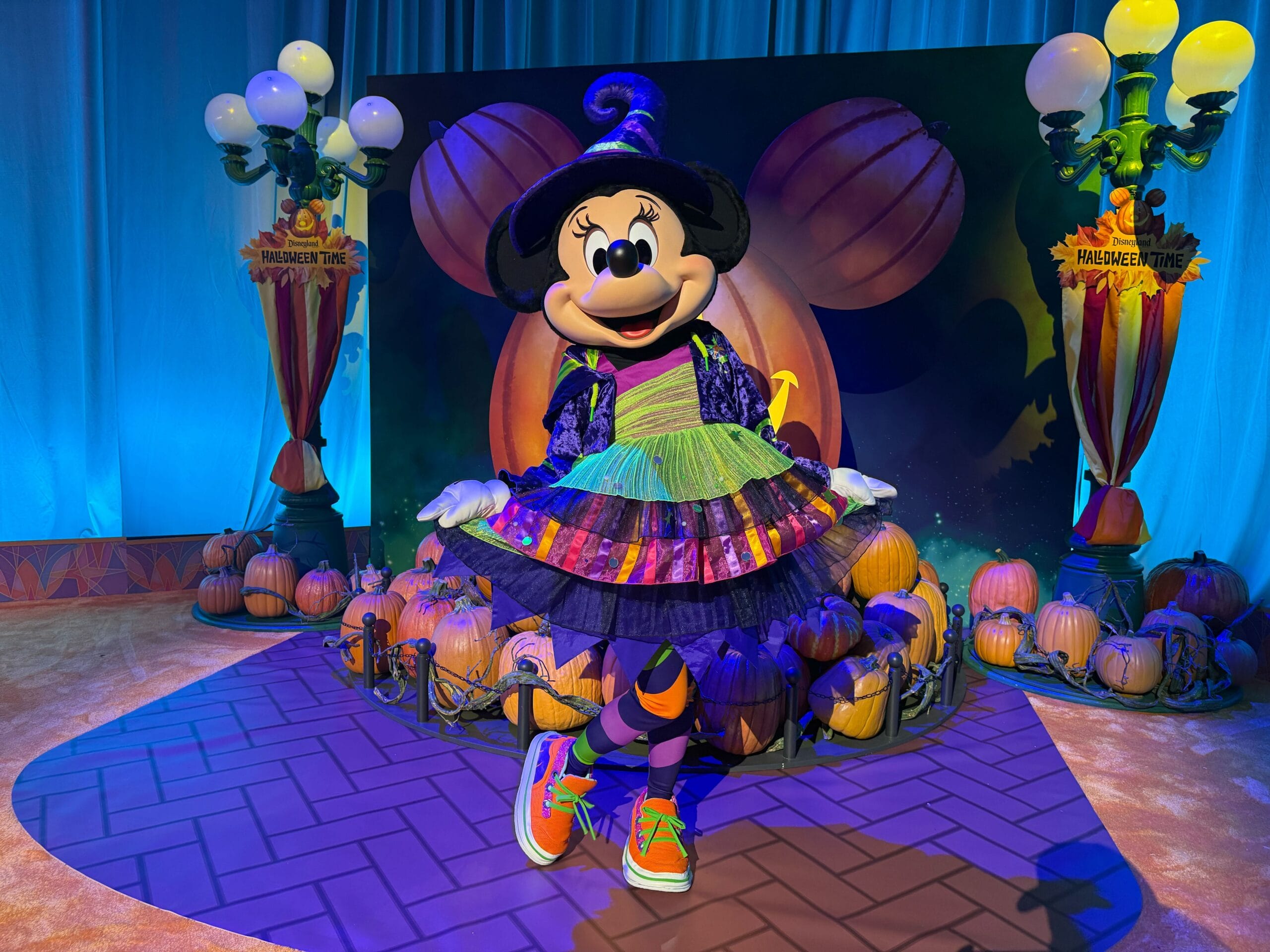 Minnie Mouse in a colorful witch costume poses with pumpkins at Disneyland’s Mickey and Friends Halloween 2025 display.