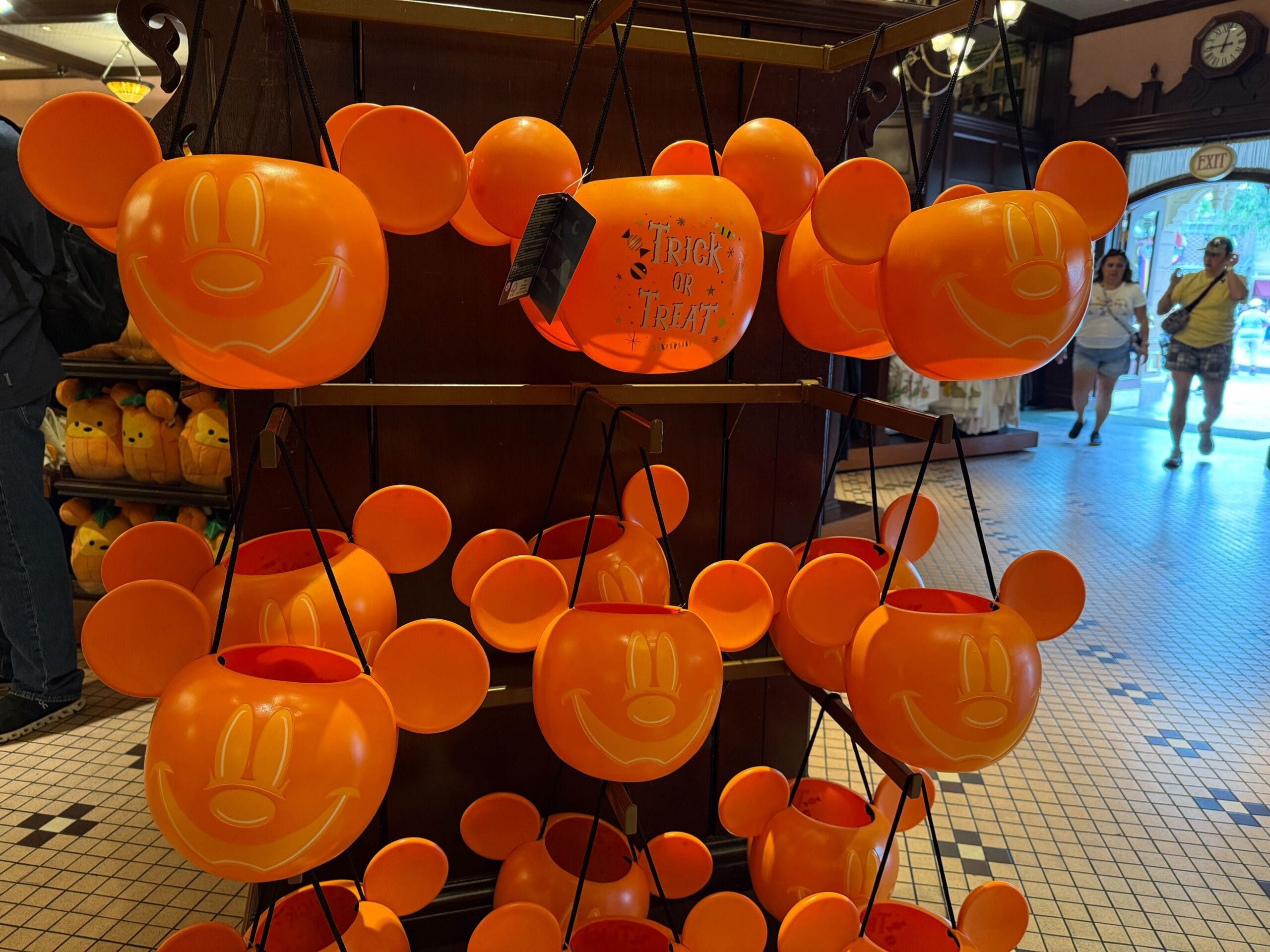 Orange Mickey Mouse-shaped Halloween buckets hanging on a display in a store, with people in the background.