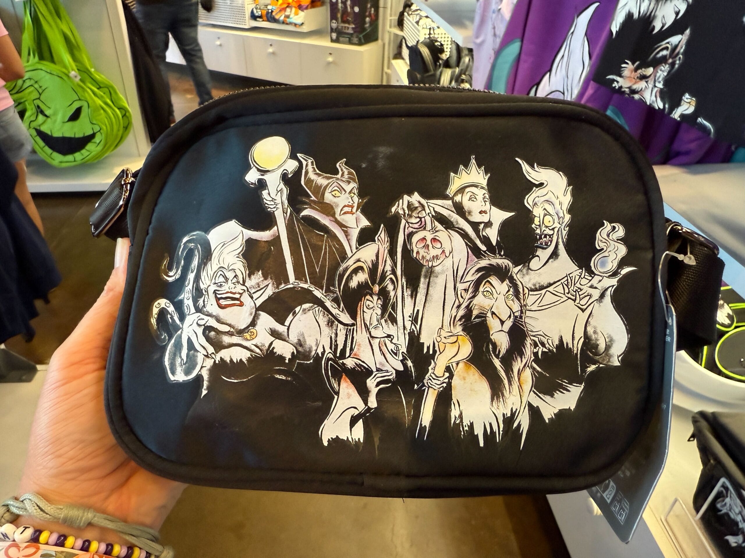 A black Villains Apparel bag with Disney villains, held in-store by someone wearing bracelets—perfect Disneyland Resort merchandise.
