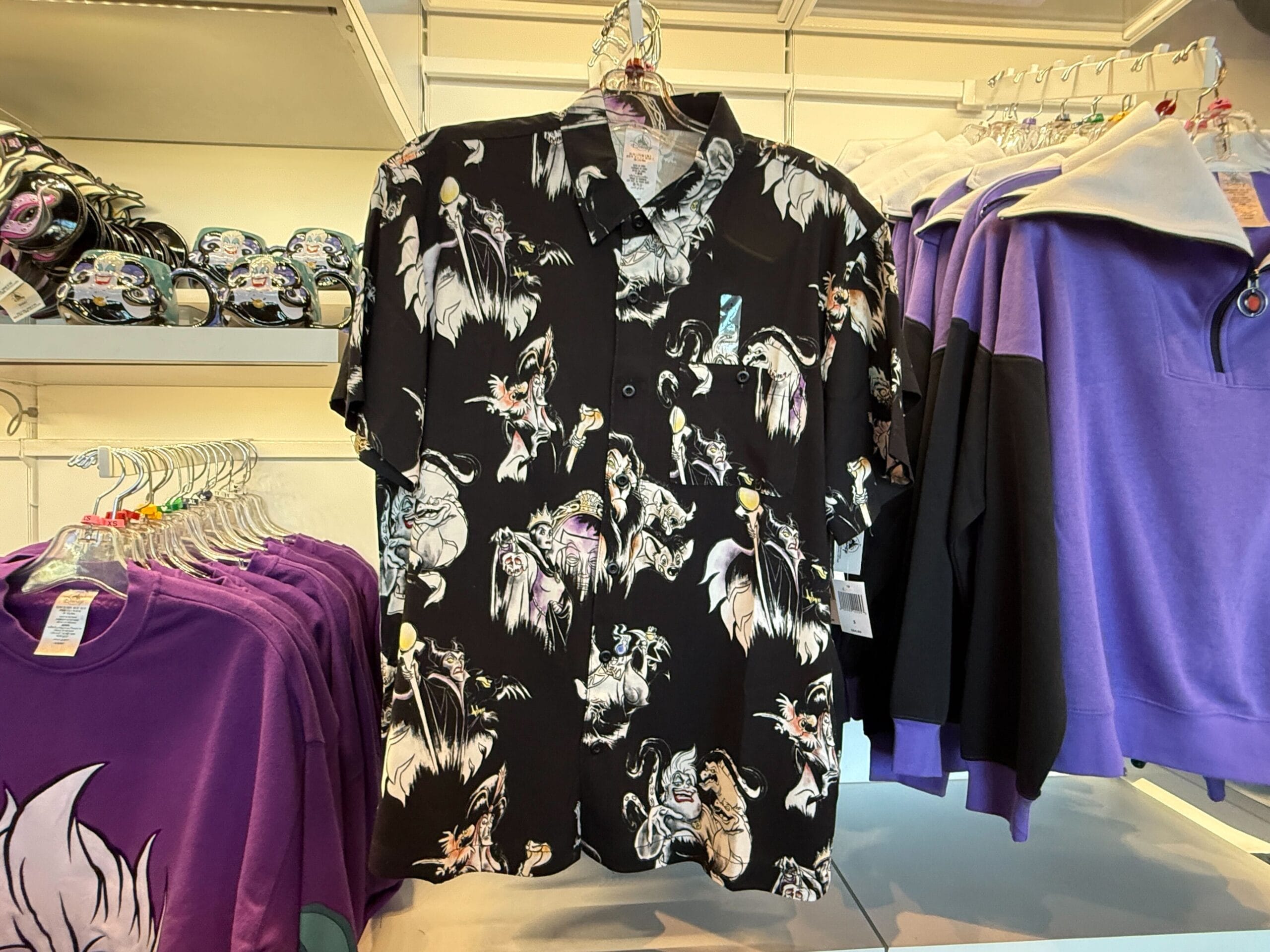 Black button-up shirt featuring Villains Apparel, hanging in a store among colorful Disneyland Resort merchandise.