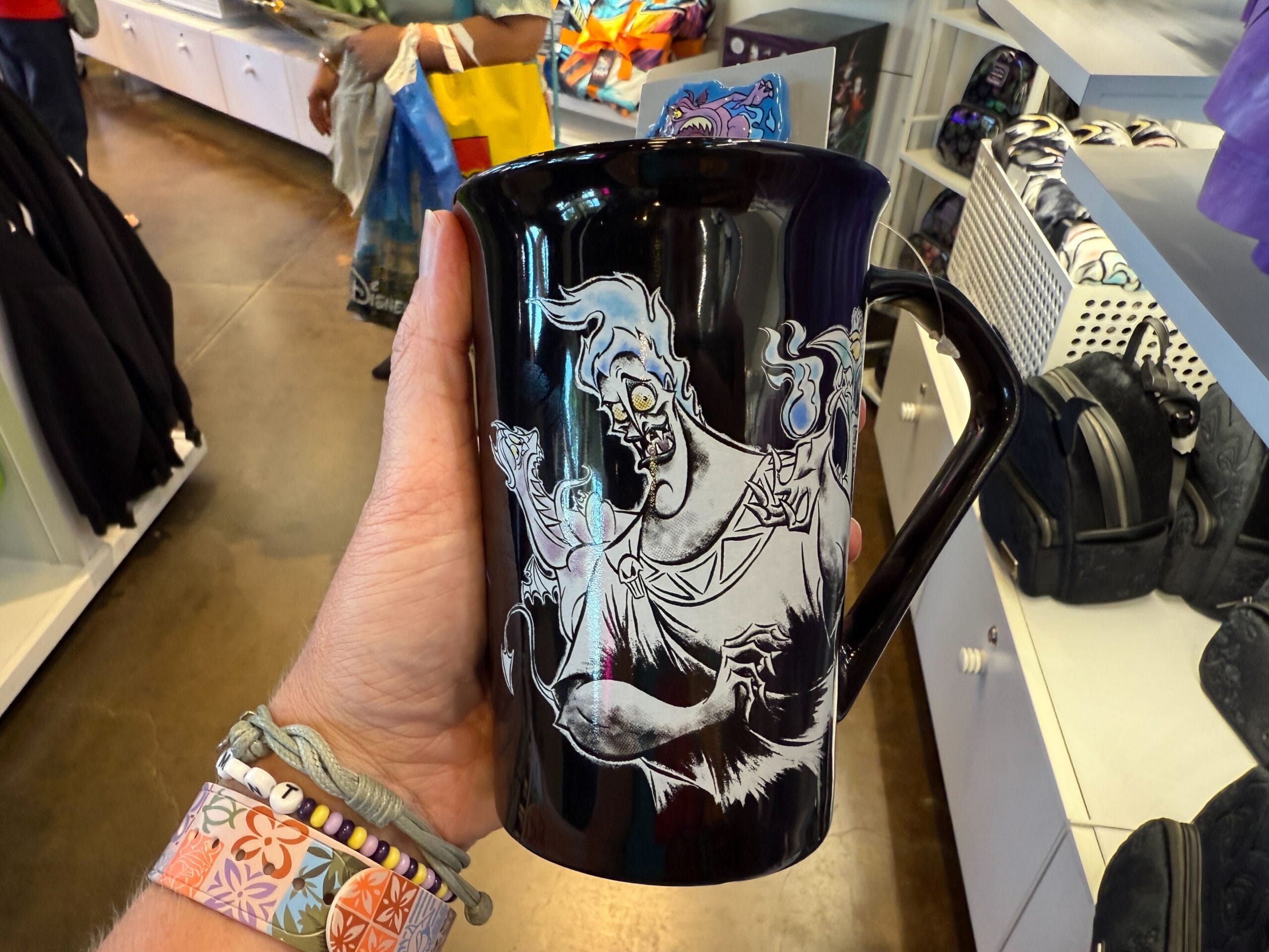 A hand holds a black mug with cartoon Hades from Disney’s Hercules—perfect Villains apparel at the Disneyland Resort.