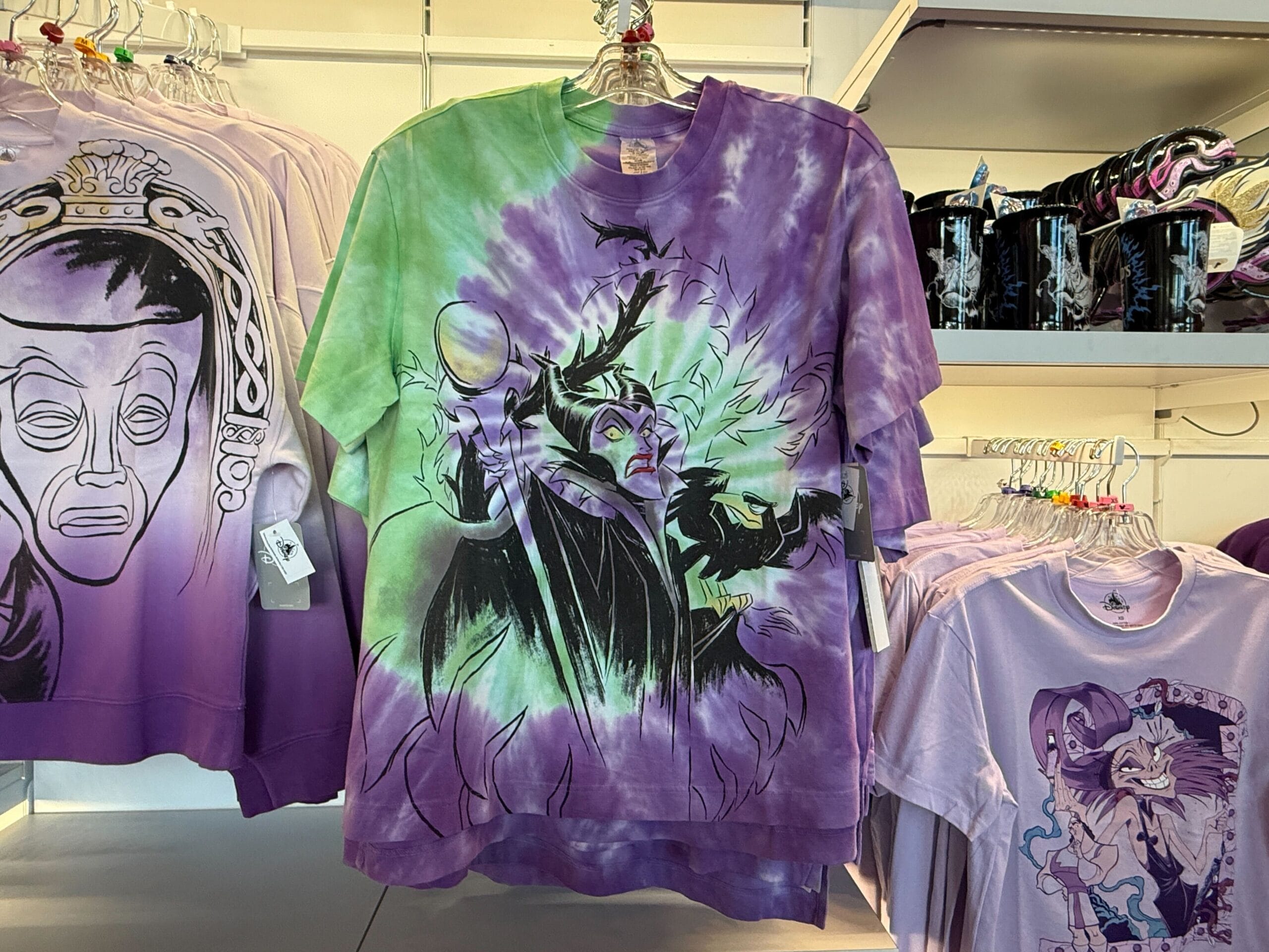 Tie-dye T-shirt from Villains Apparel featuring Maleficent in green and purple smoke, hanging on a store rack.