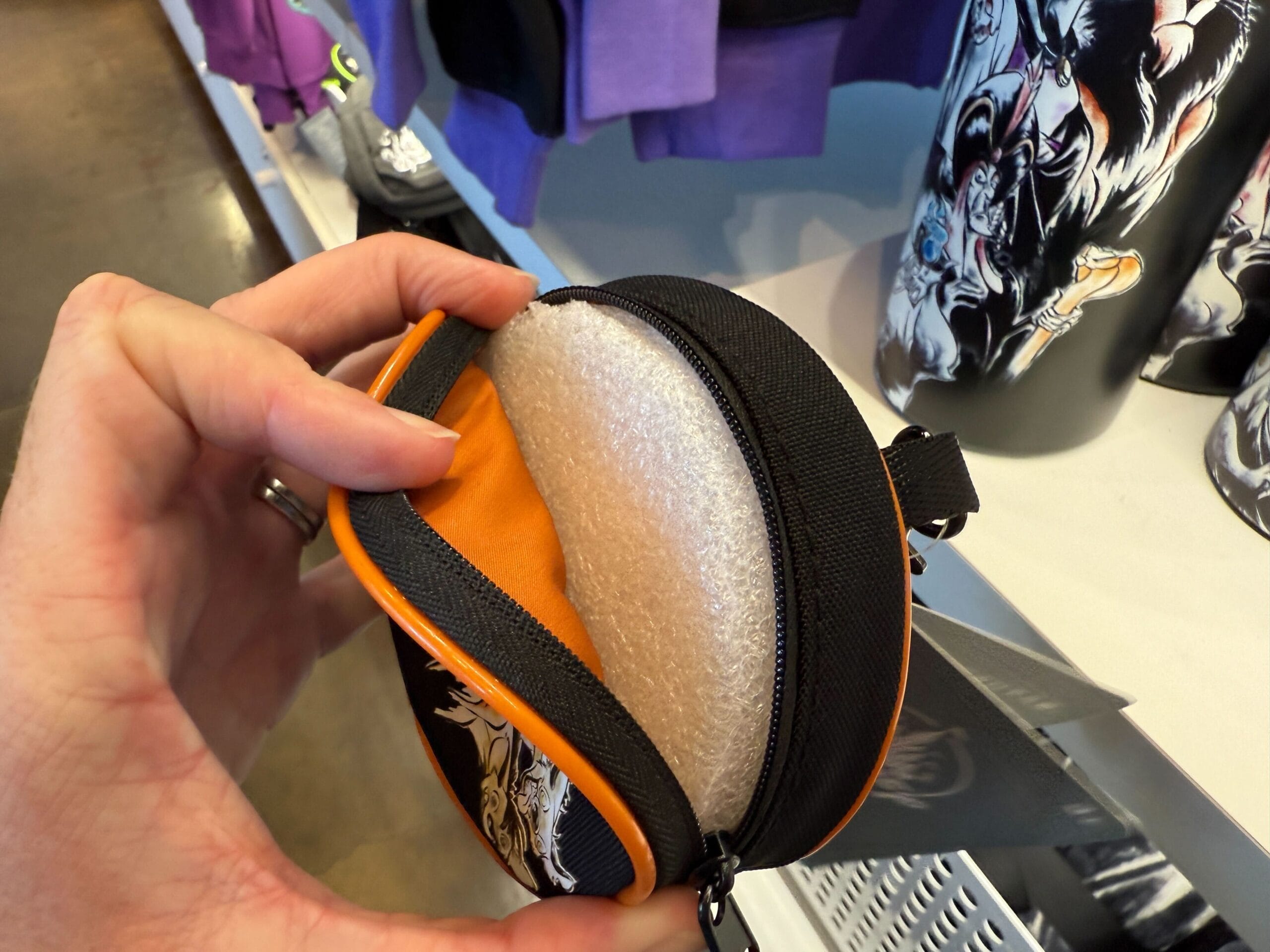 A hand holds a Villains Apparel zippered pouch with a white foam insert, spotted at the Disneyland Resort merchandise store.