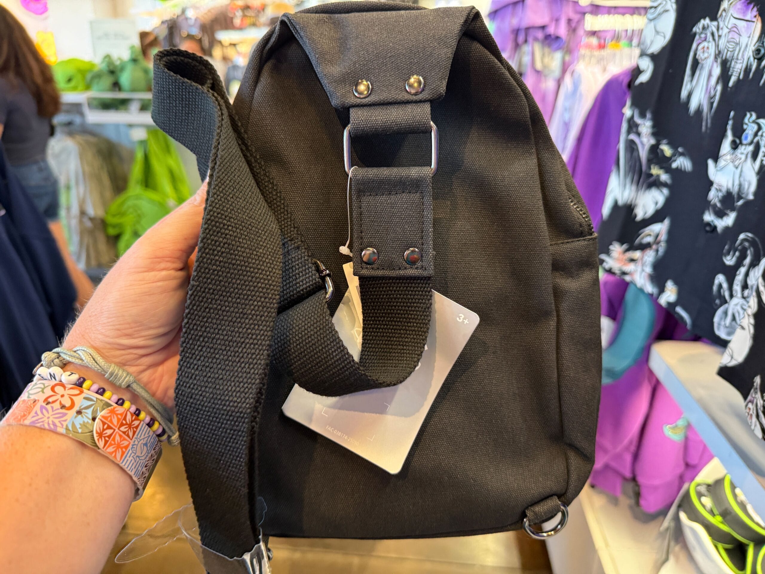 A hand holds a small black backpack in a clothing store, surrounded by colorful Villains Apparel merchandise.