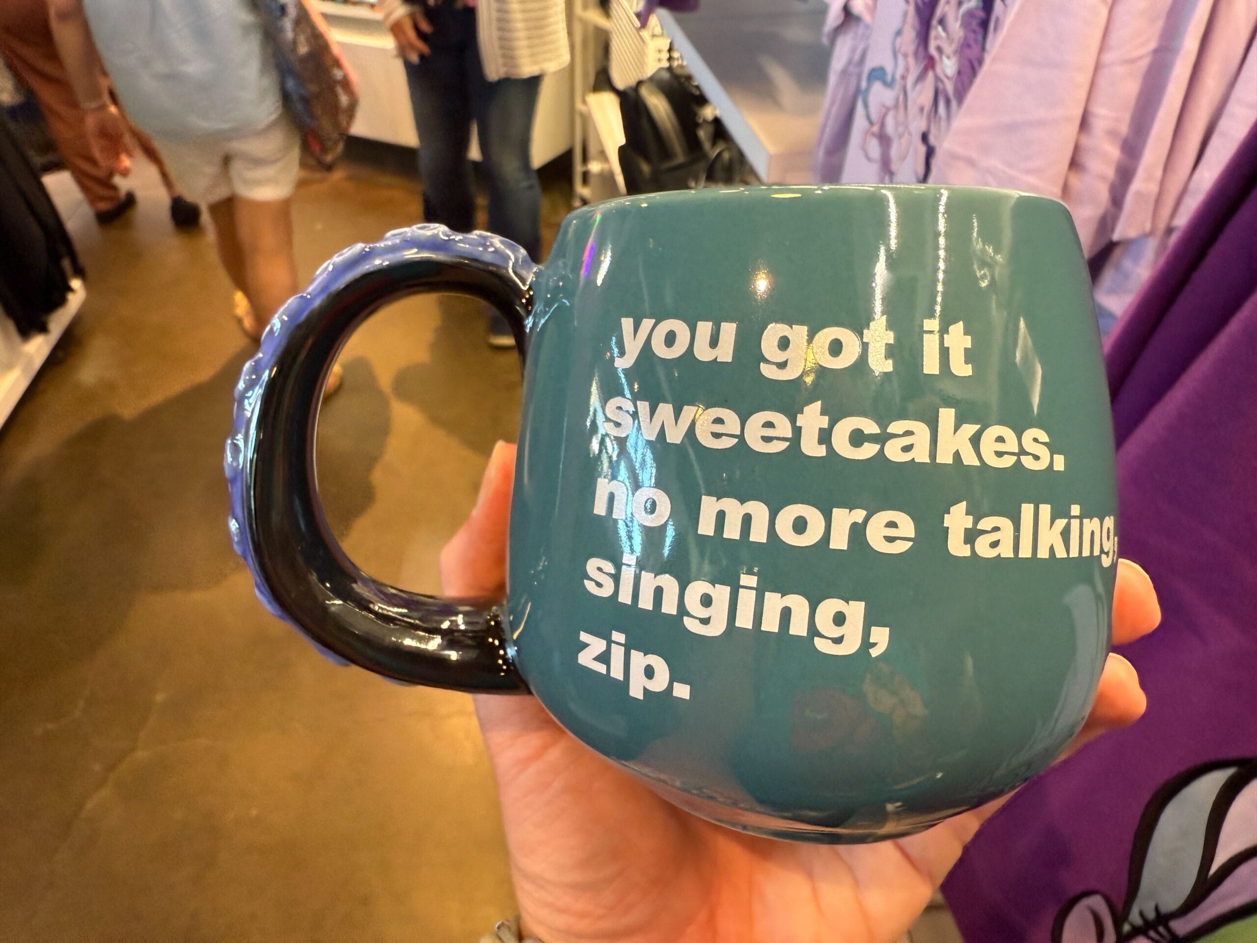 A teal mug from Villains apparel with “you got it sweetcakes. no more talking, singing, zip.” printed in white text.