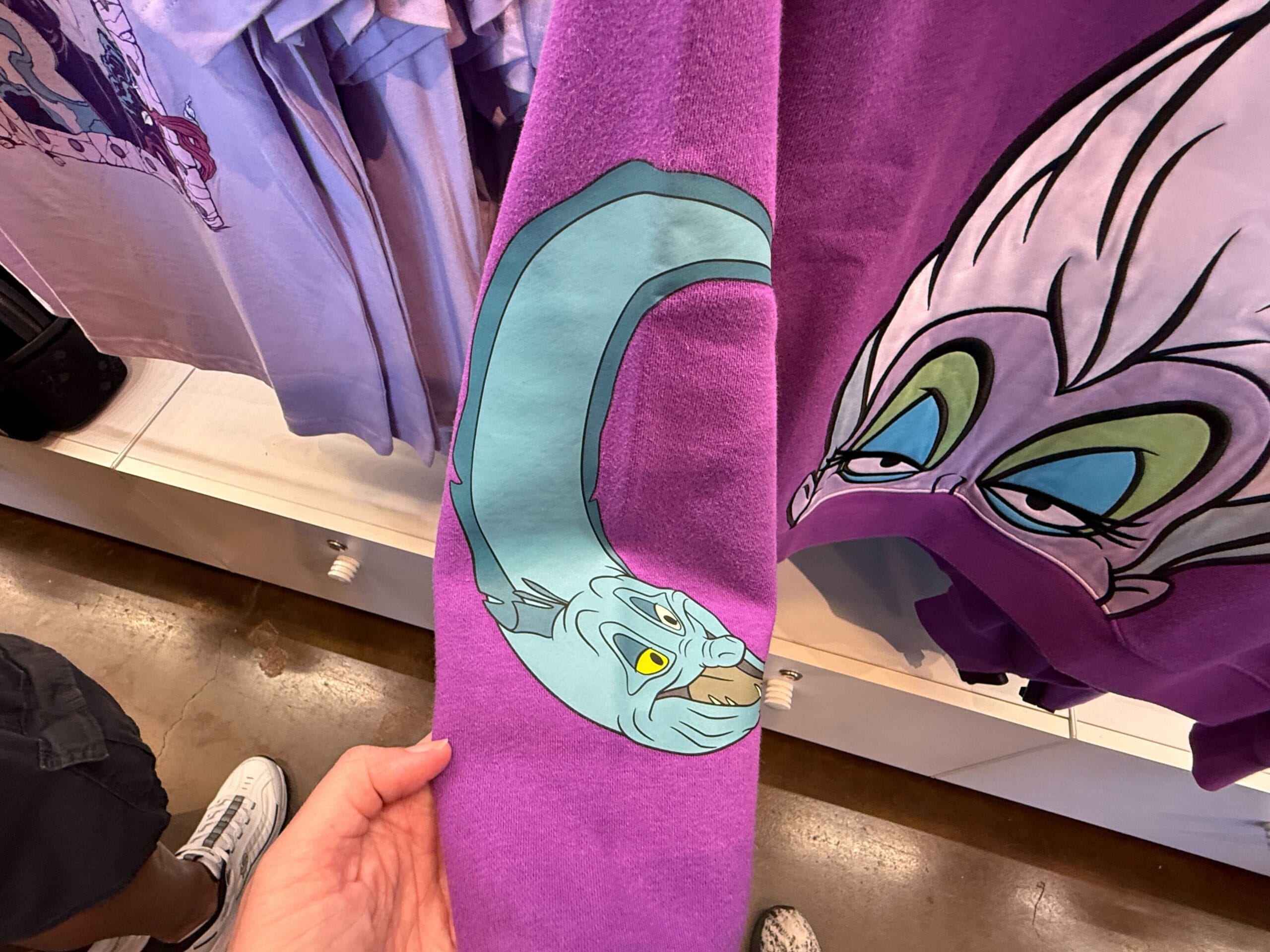 A purple sweatshirt with Ursula’s face and a blue eel graphic, perfect for villains merchandise at Disneyland Resort.