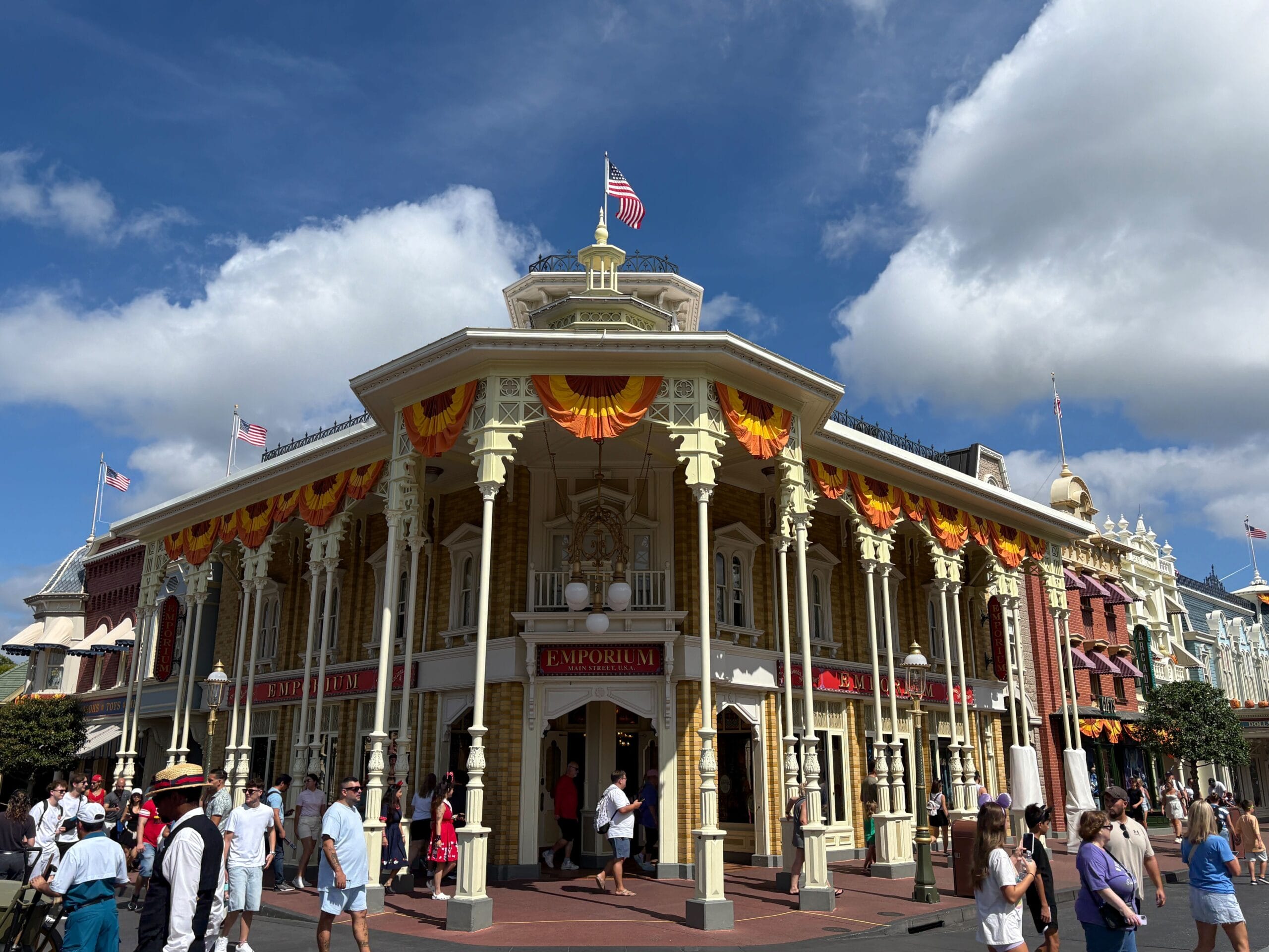 Victorian-style building with Halloween decor, people walking in front under a blue sky at Magic Kingdom.