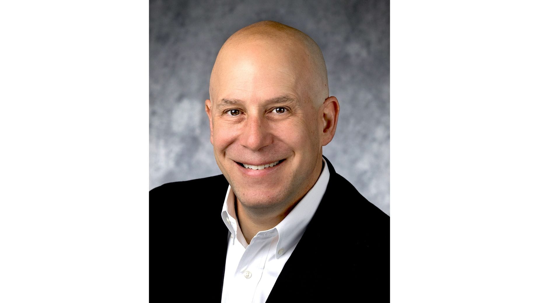 Smiling bald man in a suit jacket and white shirt, Disney Creative Consultant, against a gray mottled background.