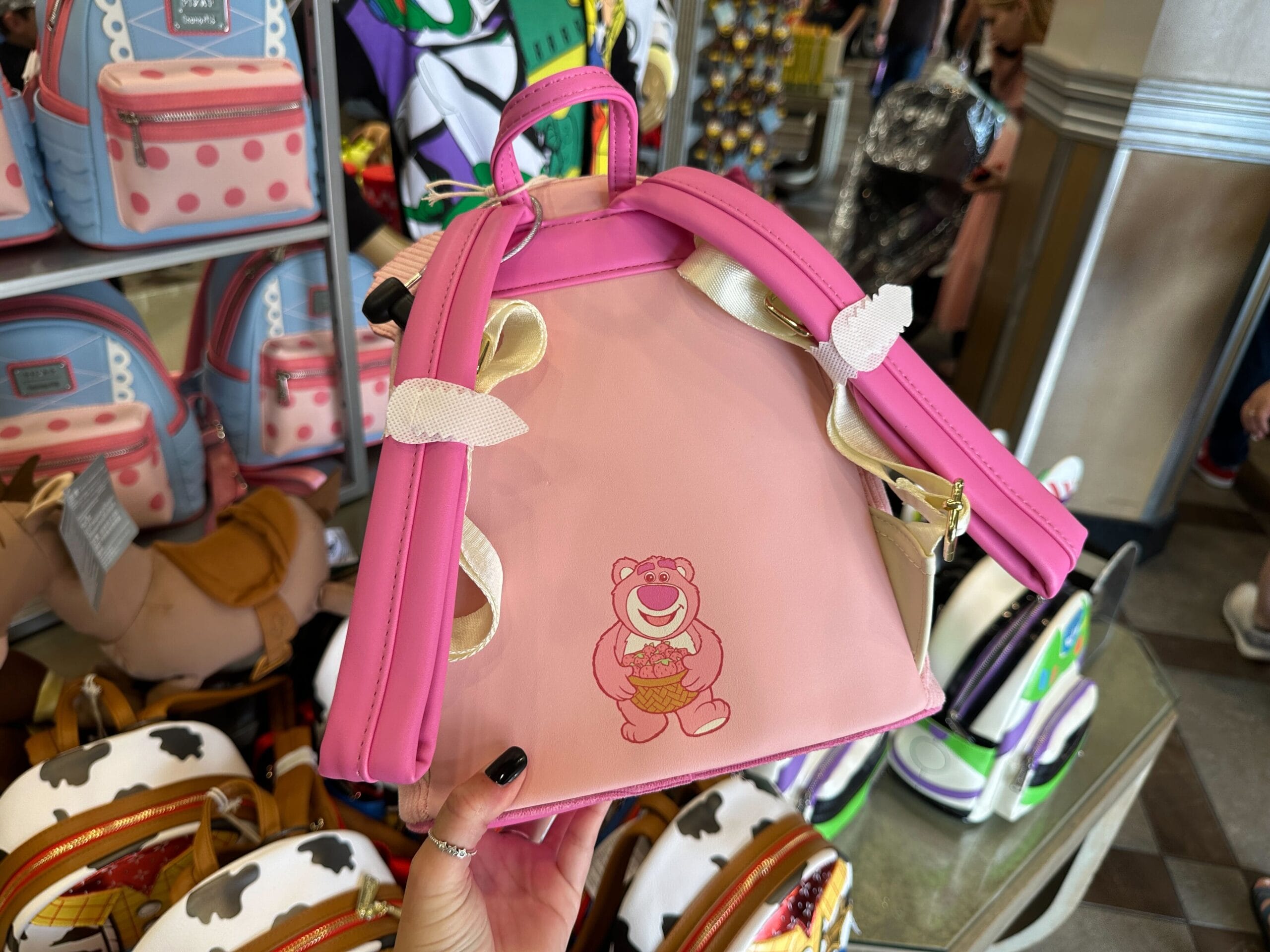 A scented Lotso Loungefly Backpack with strawberries, displayed among character bags at Disney's Hollywood Studios.