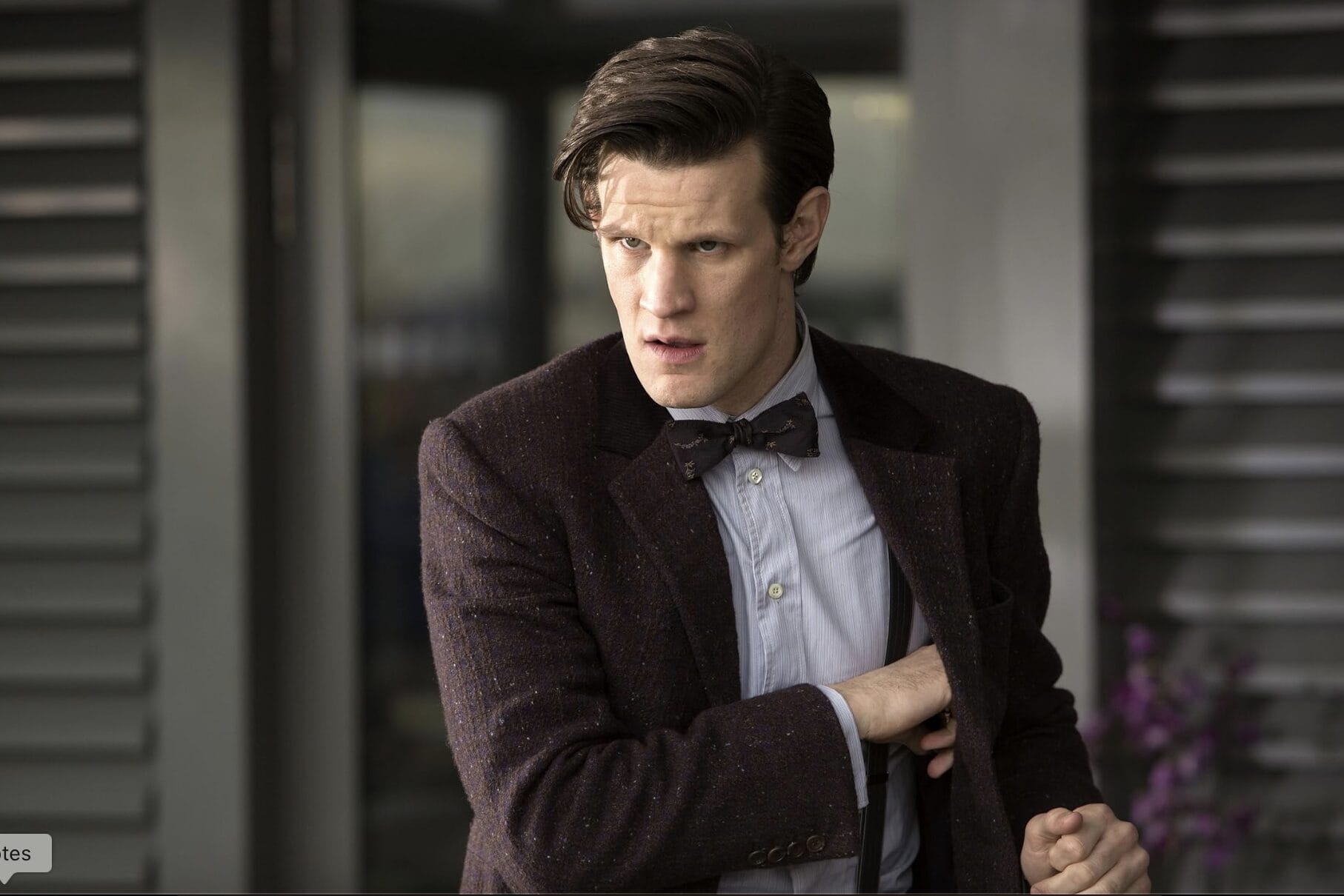 A man with styled brown hair in a bow tie and dark jacket stands, looking serious—like Matt Smith as a Star Wars starfighter pilot.