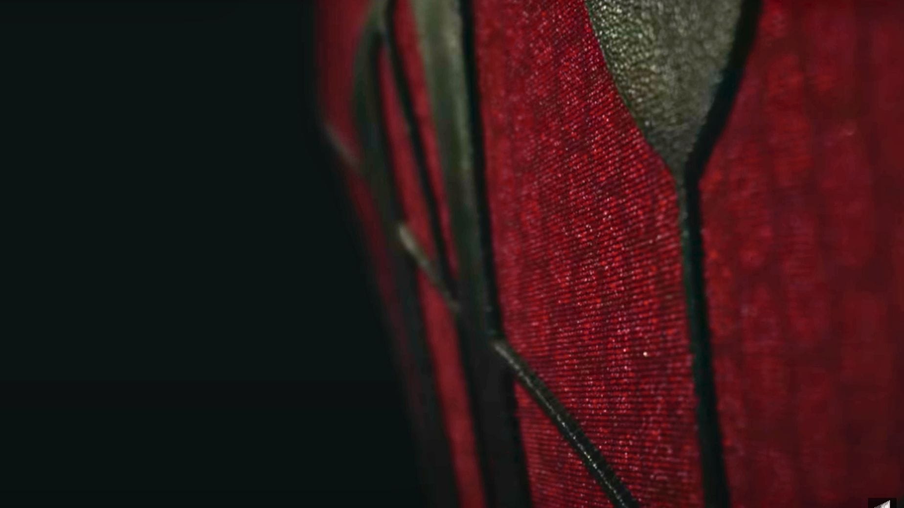 Close-up teaser of Spider-Man's red and black textured suit with angular patterns against a dark background.