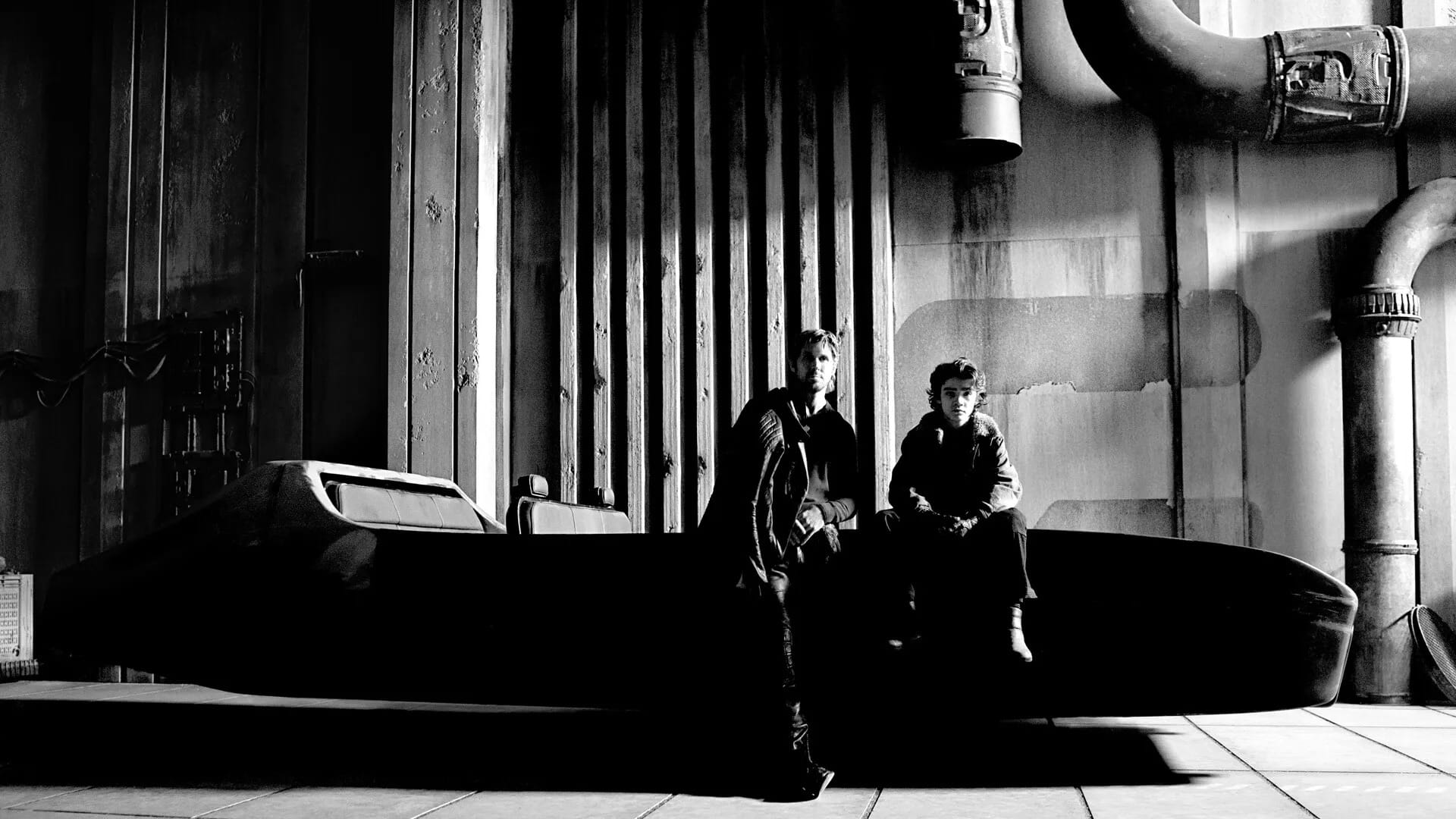 Two people in dark clothing stand beside a Star Wars-style starfighter in an industrial, shadowy setting.