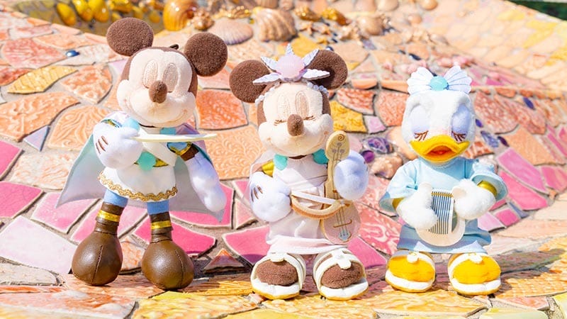 Three plush dolls of Mickey, Minnie, and Daisy in pastel kimonos, posed on colorful mosaic tiles.