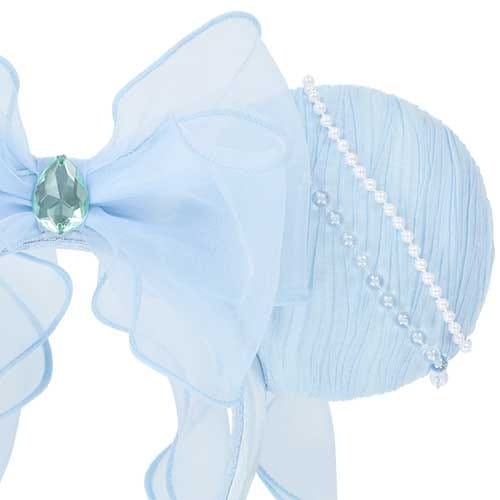 Light blue decorative bow with a green gem and pearls on a textured circular background.