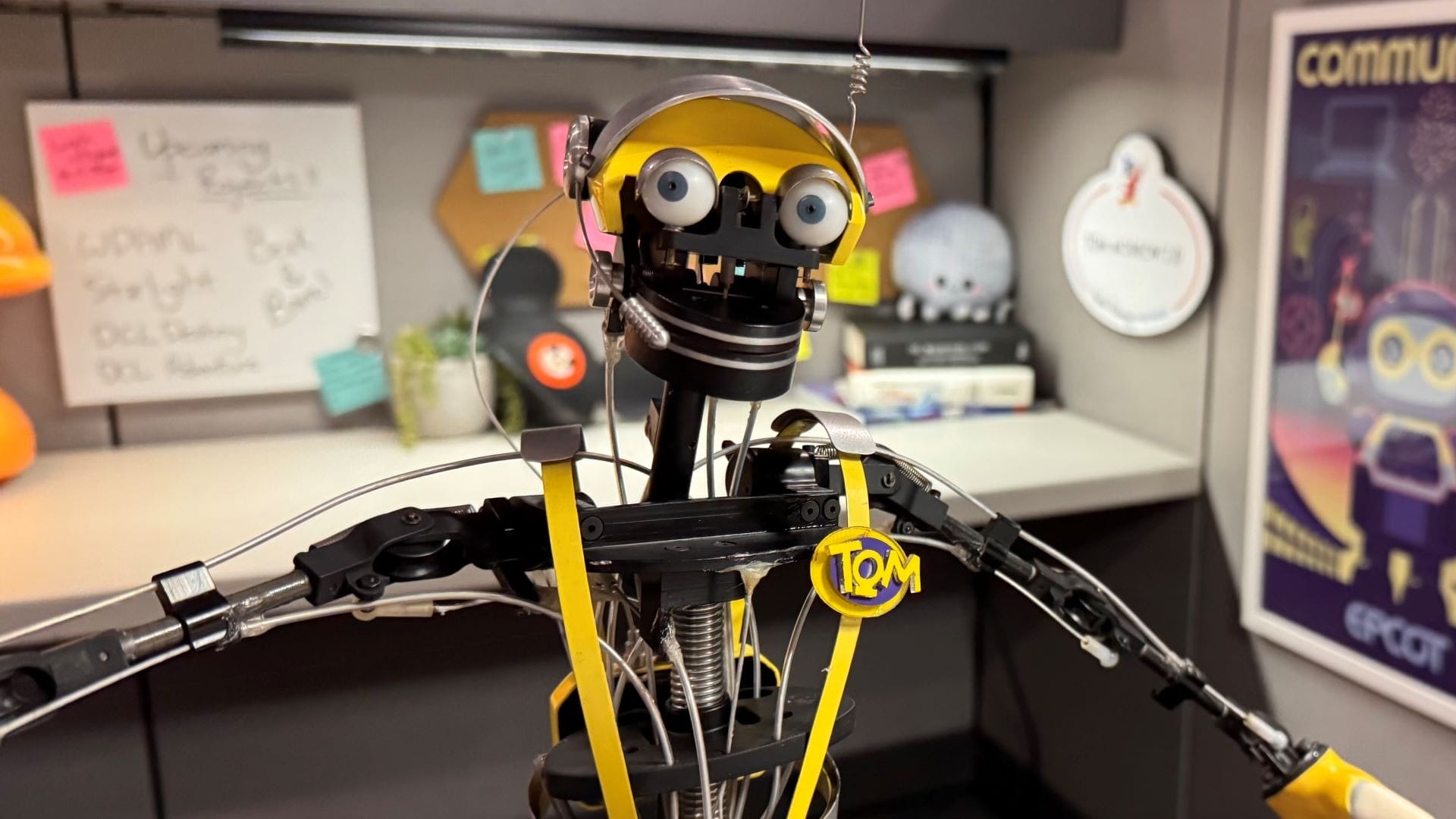 A yellow robot with exposed wires and gears stands in an office cubicle, ready to Imagineer That.