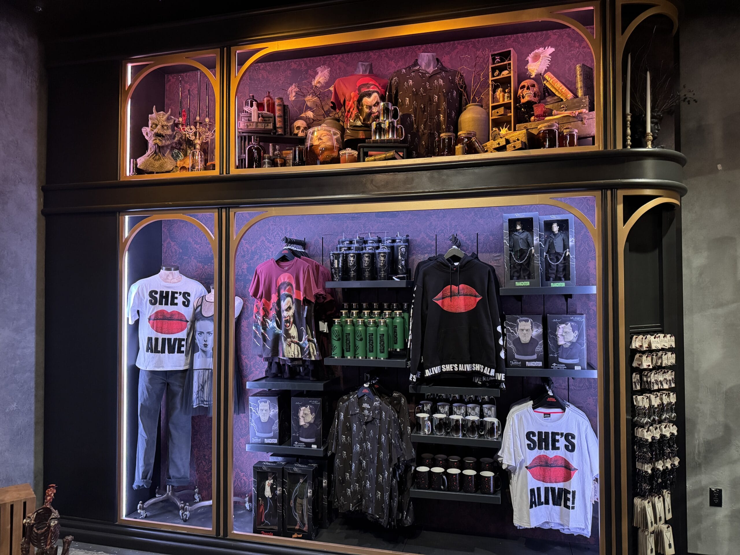 Store display with Universal Horror Unleashed shirts and decor, including "She's Alive!" tops and monster figurines in Las Vegas.