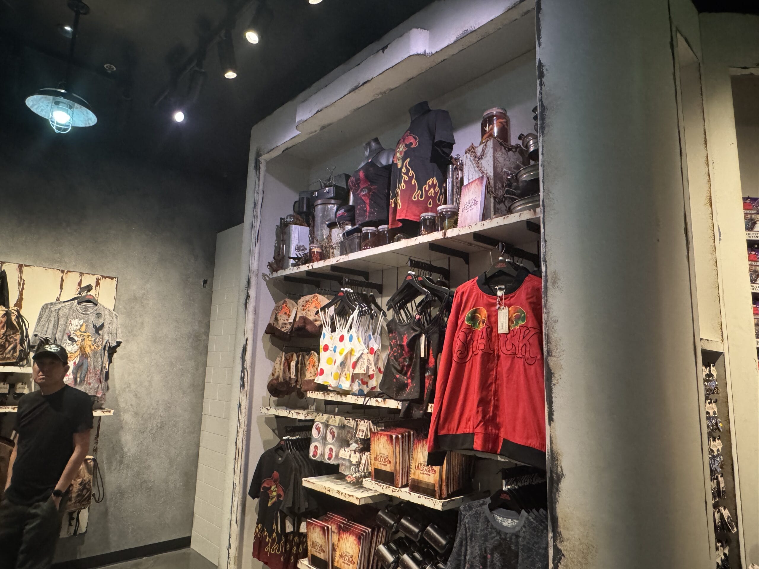 A store display with Universal Horror Unleashed T-shirts, mugs, and merchandise on shelves; a person stands to the left.