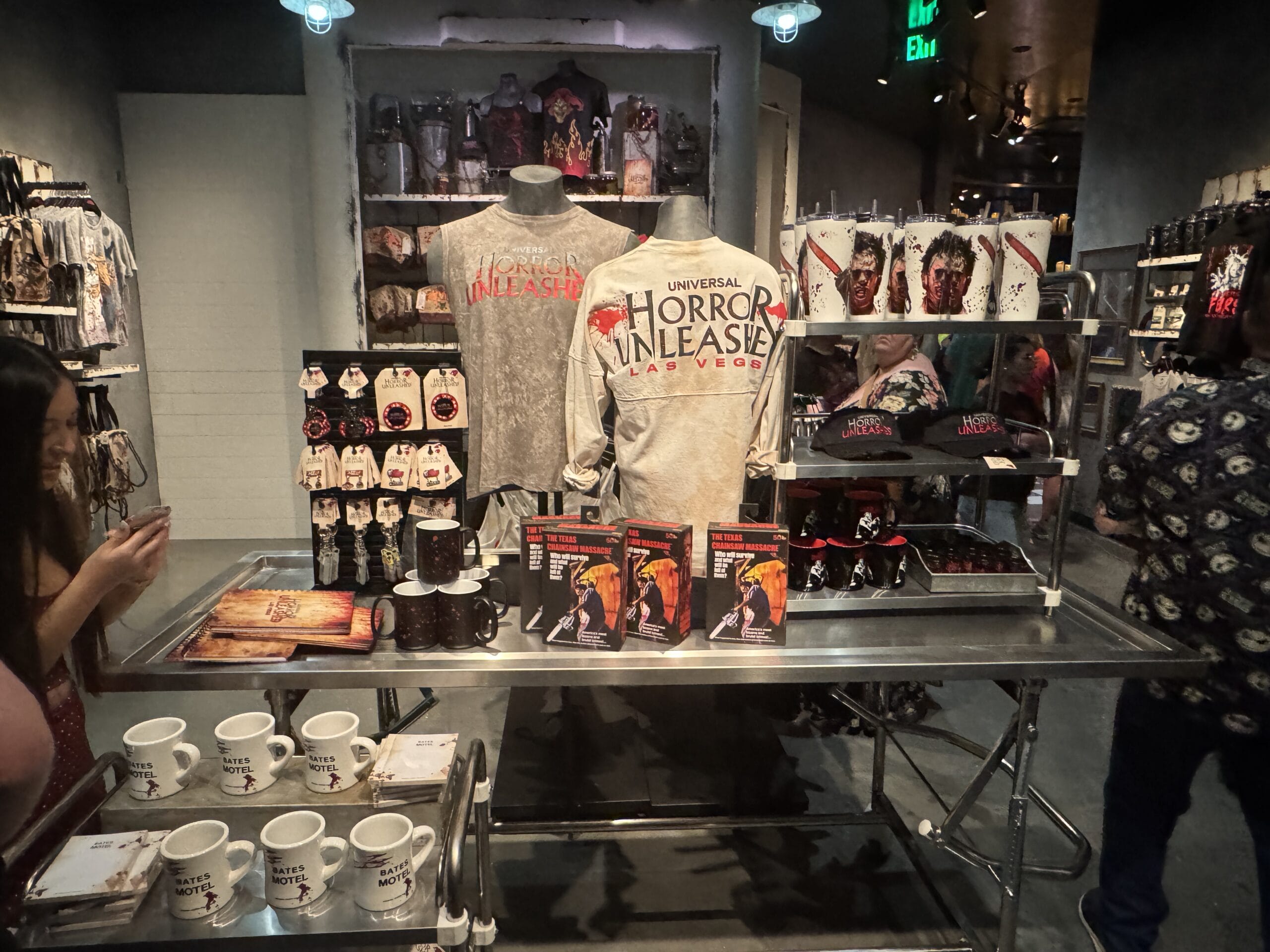Merchandise display at Universal Horror Unleashed Las Vegas, featuring shirts, mugs, hats, and horror-themed souvenirs.