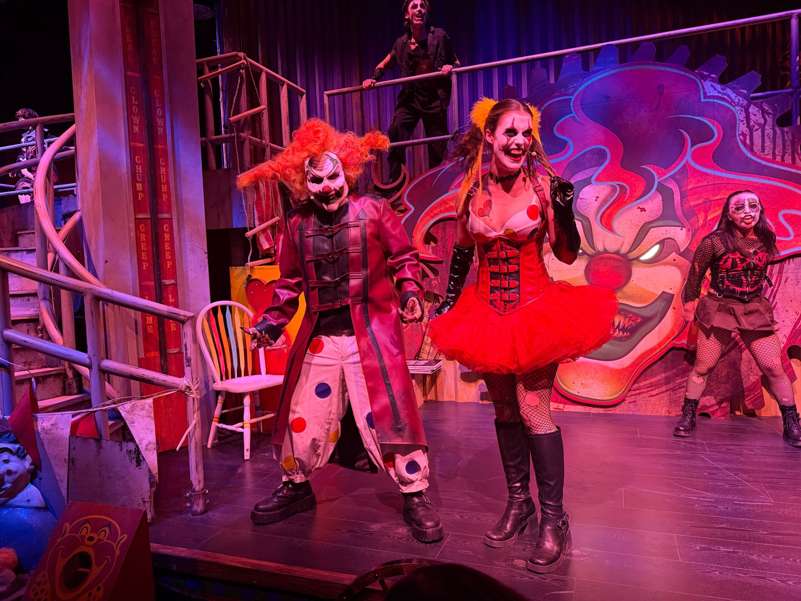 Performers in creepy clown costumes dance on a circus stage as Jack and Chance loom in the clown face art background.