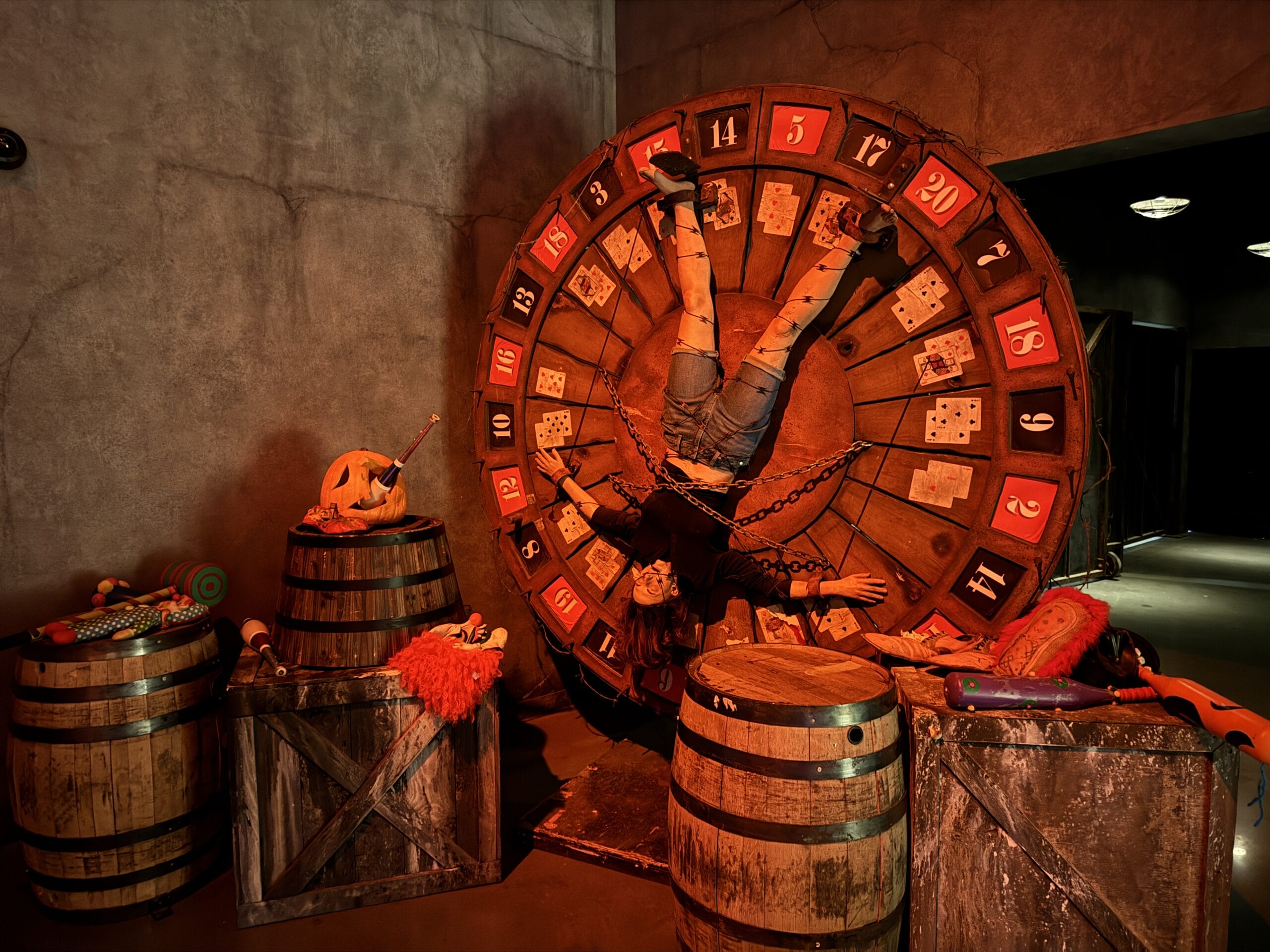 A person is strapped upside down to a spinning wheel at Universal Horror Unleashed, Las Vegas, surrounded by Halloween props.