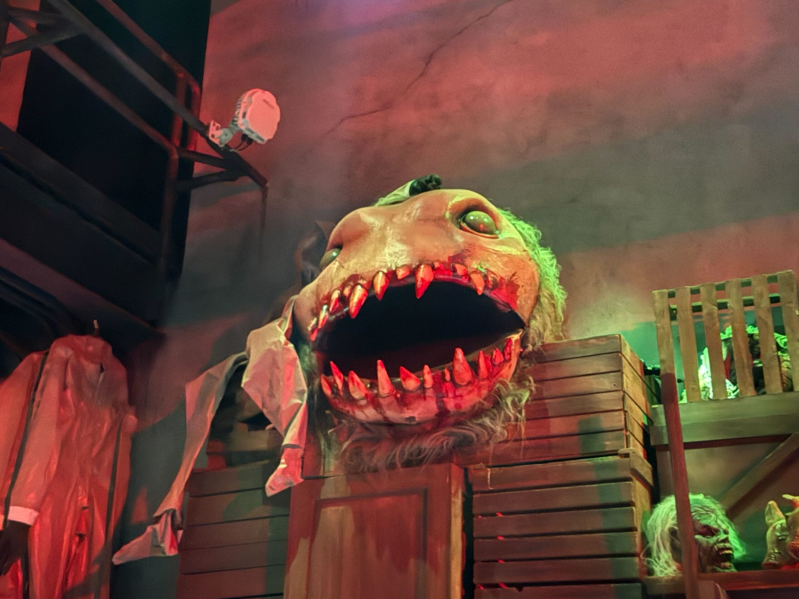 A large, monster head with sharp teeth sits among crates in a spooky room—Universal Horror Unleashed in Las Vegas.