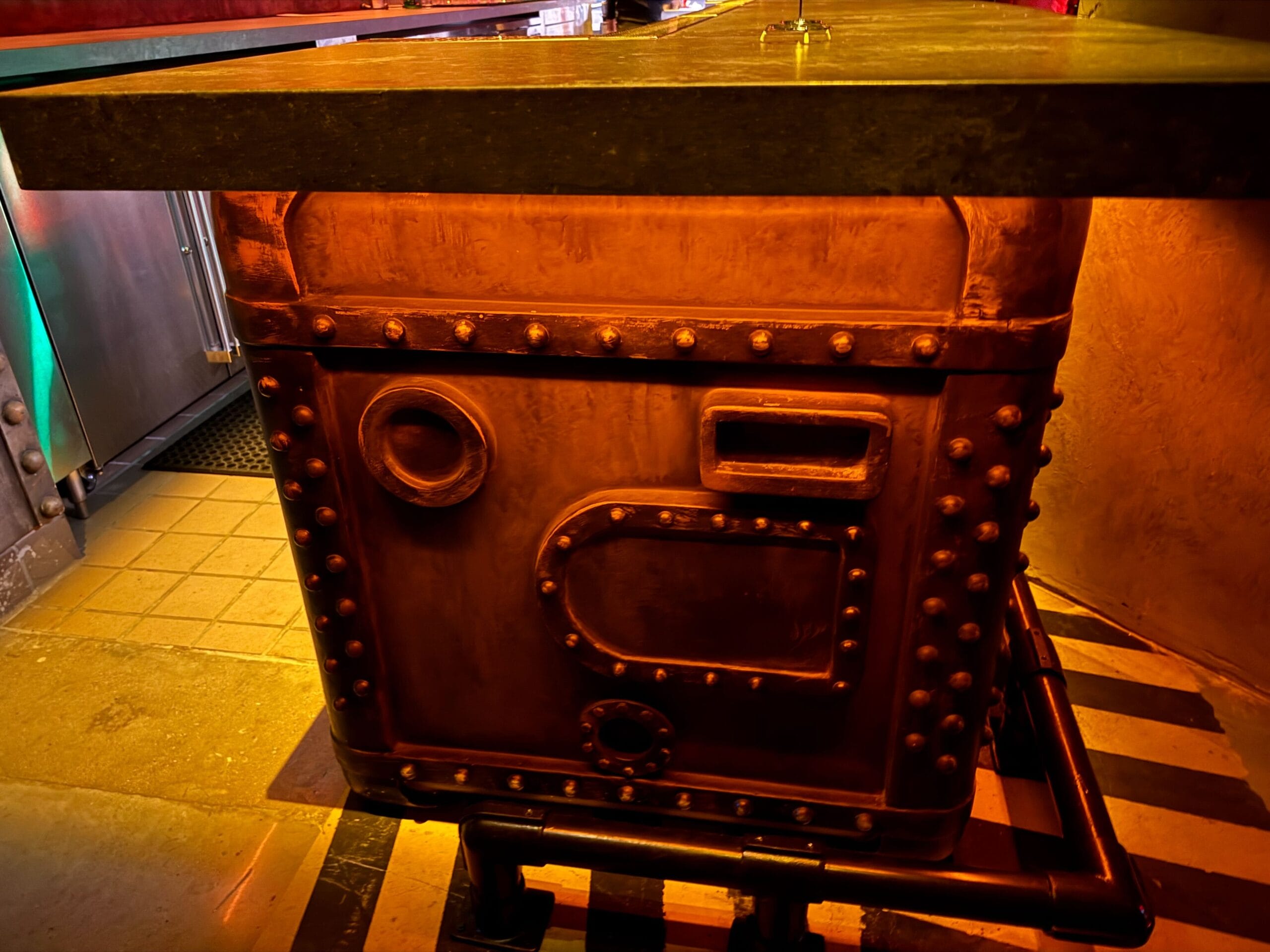 A large, riveted, industrial-style metal box supports a wooden tabletop in a dim Las Vegas room.