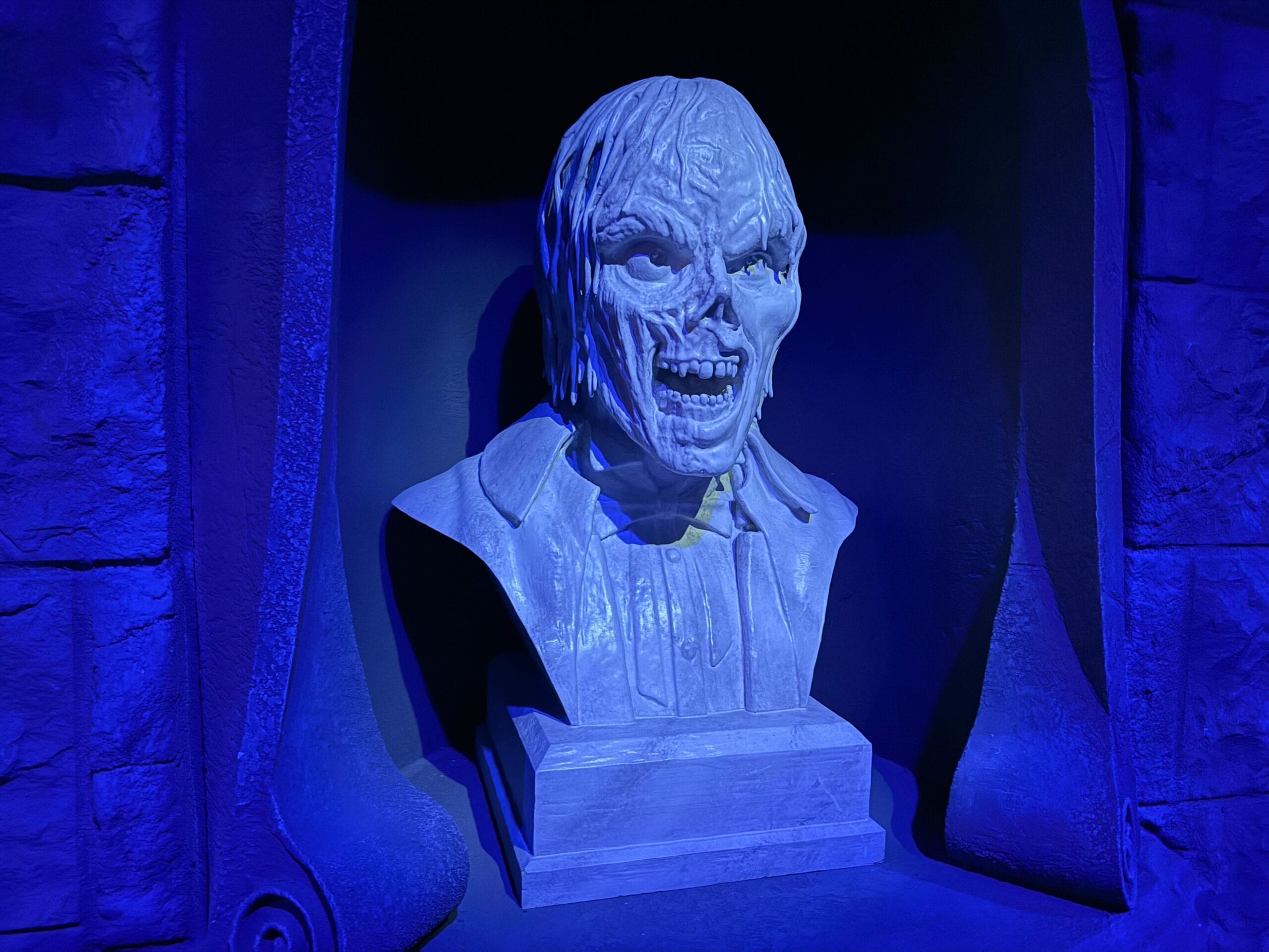 A creepy, cracked bust of a snarling man lit with blue light, like a relic from Universal Horror Unleashed.