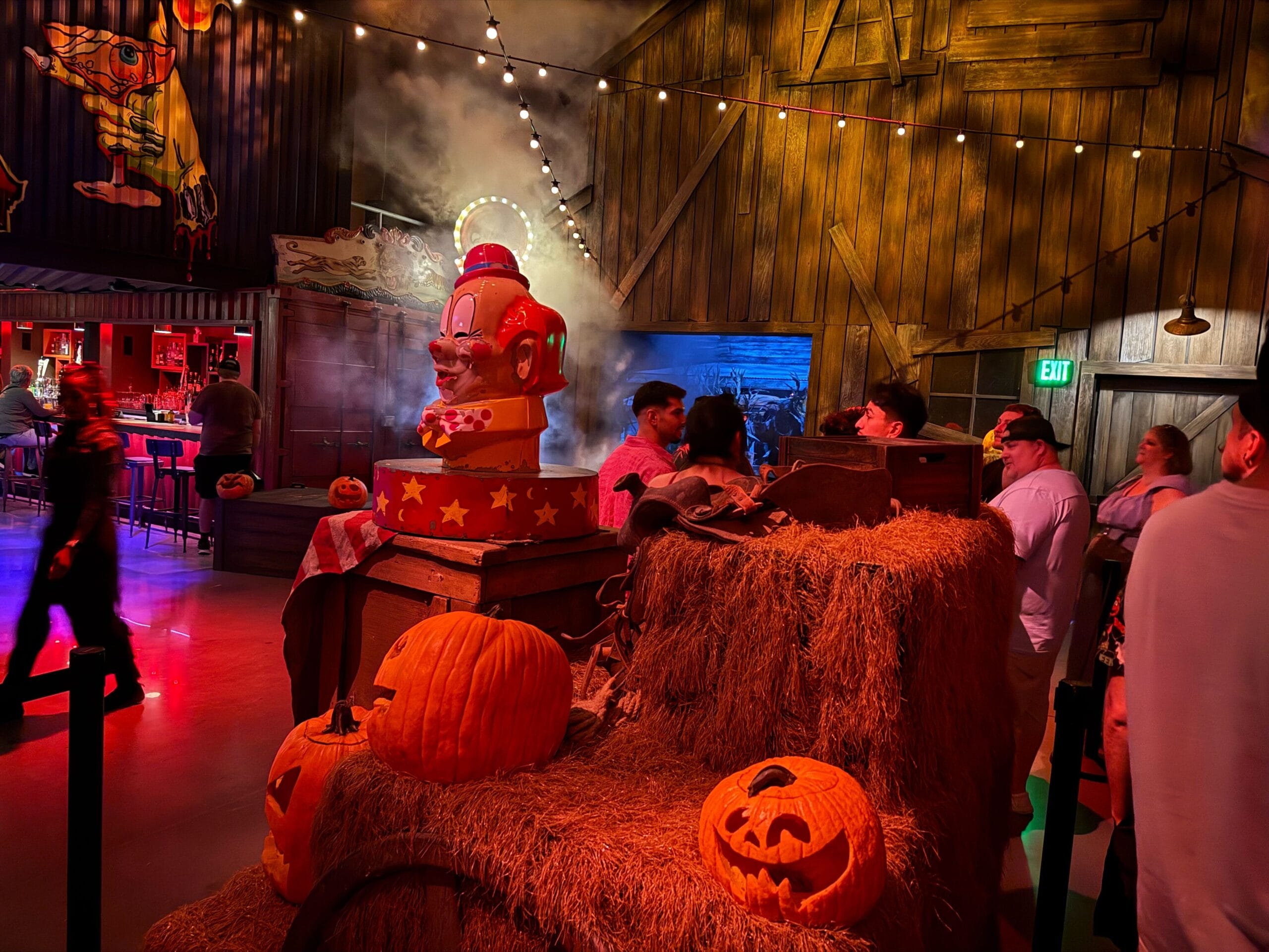 People gather in a dimly lit, Halloween-themed room inspired by Universal Horror Unleashed with jack-o'-lanterns and hay bales.