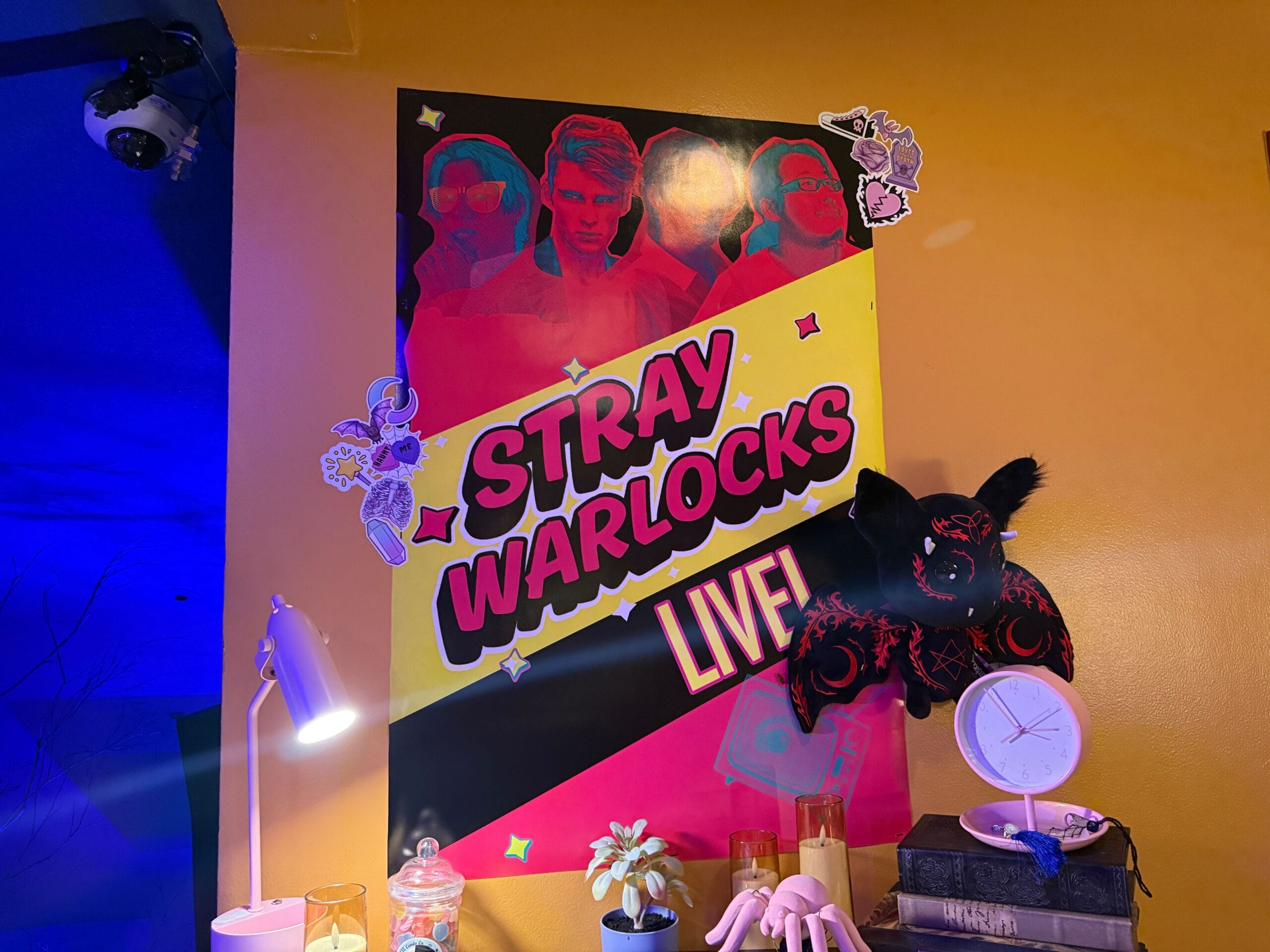 Poster on yellow wall reads "Stray Warlocks Live! Full Tour" with stylized faces, decorations, and assorted objects below.