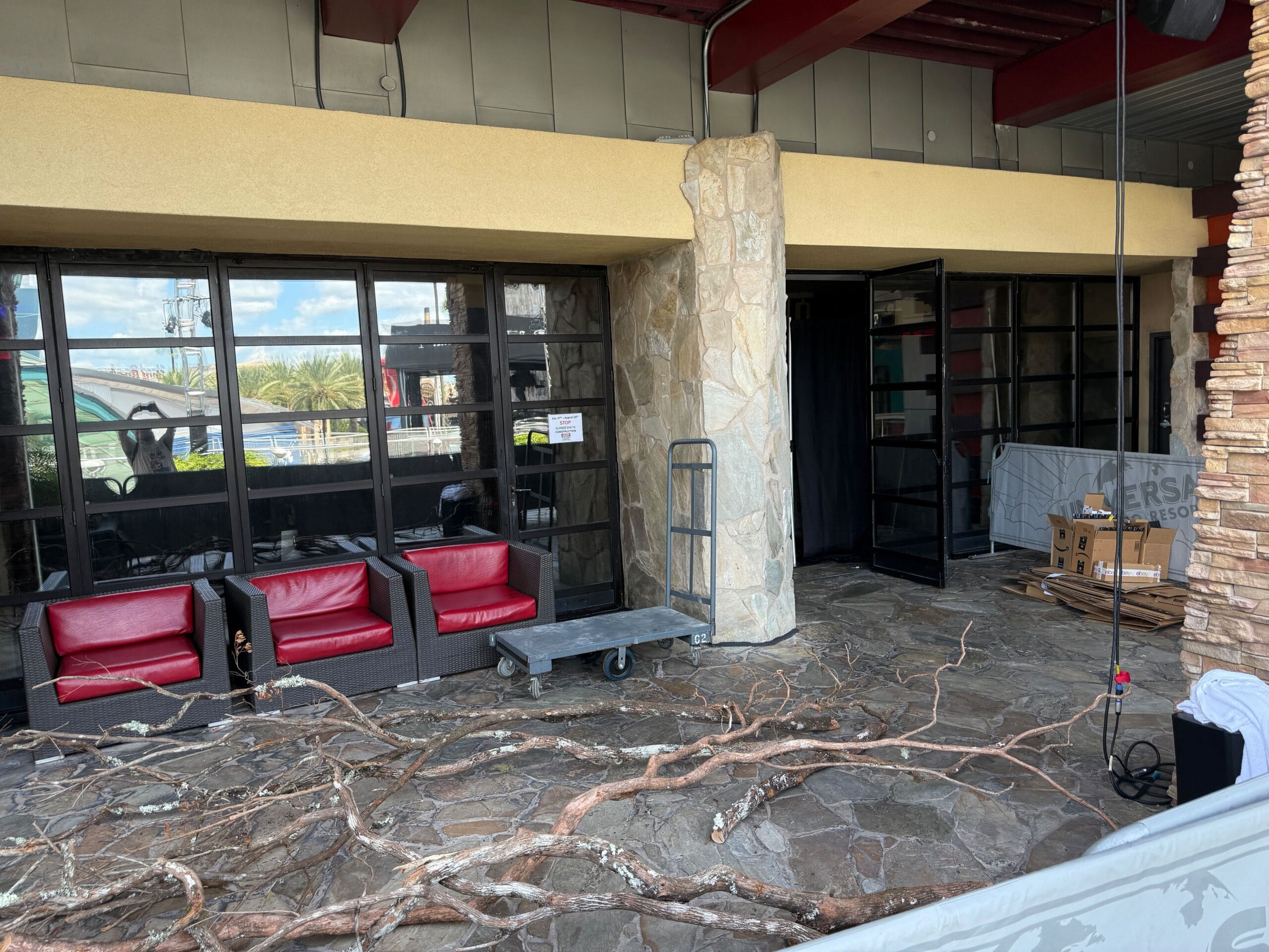 Branches on a stone patio in front of red chairs, a dolly, and glass doors outside a building.