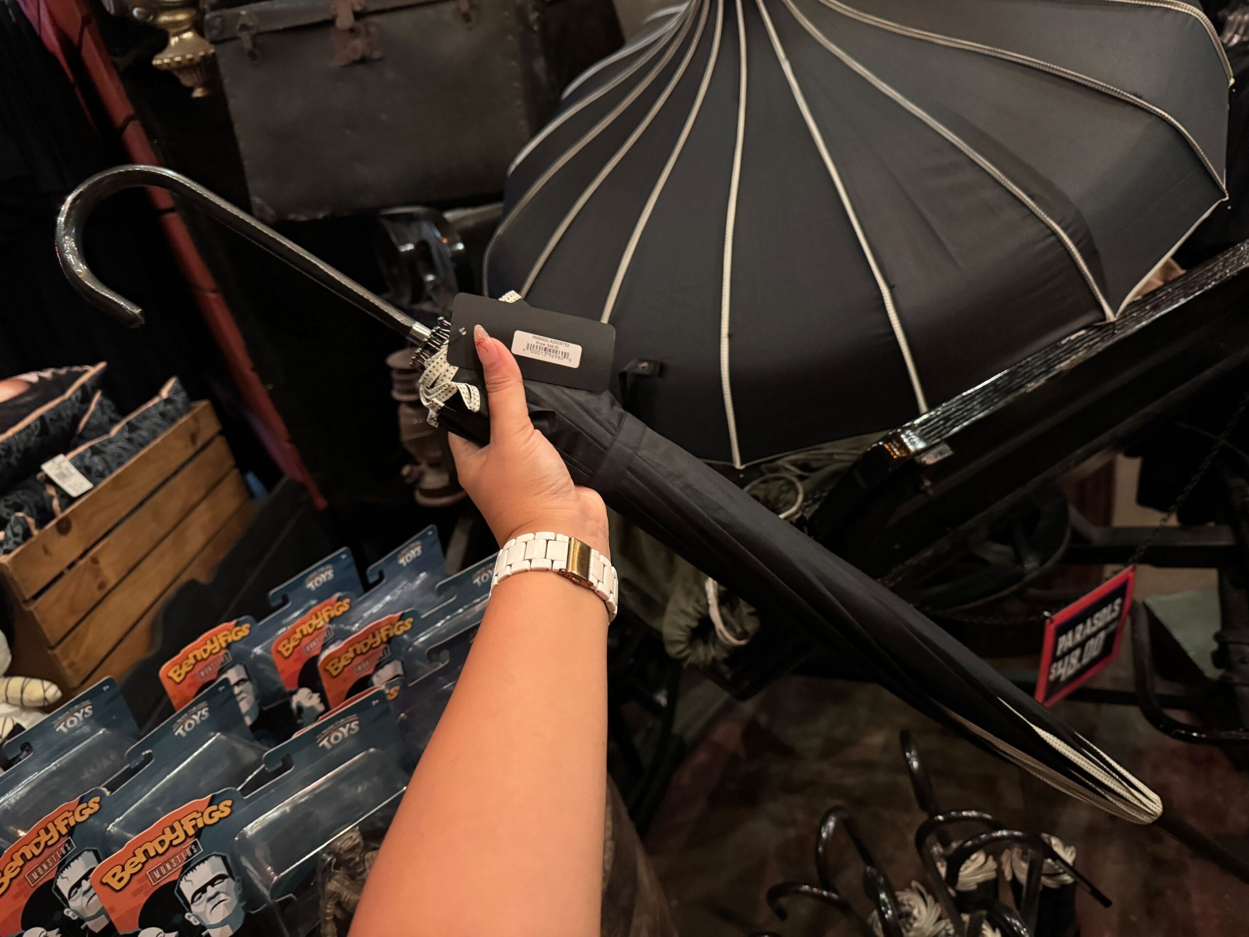 A hand holding a black umbrella with a curved handle in a store with various items and collectibles.