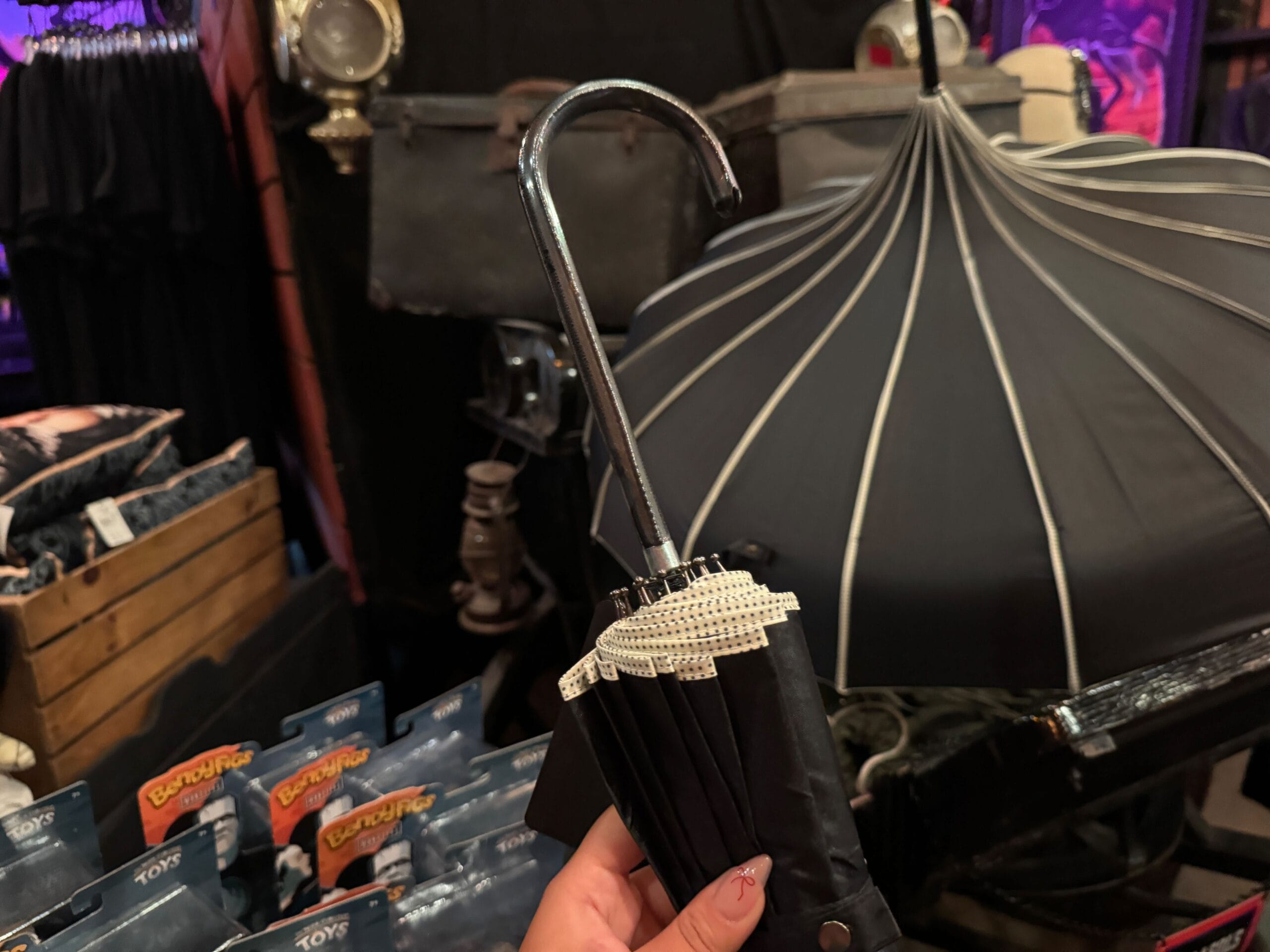 A hand holds a closed black umbrella with a silver hook handle in a store selling various items.