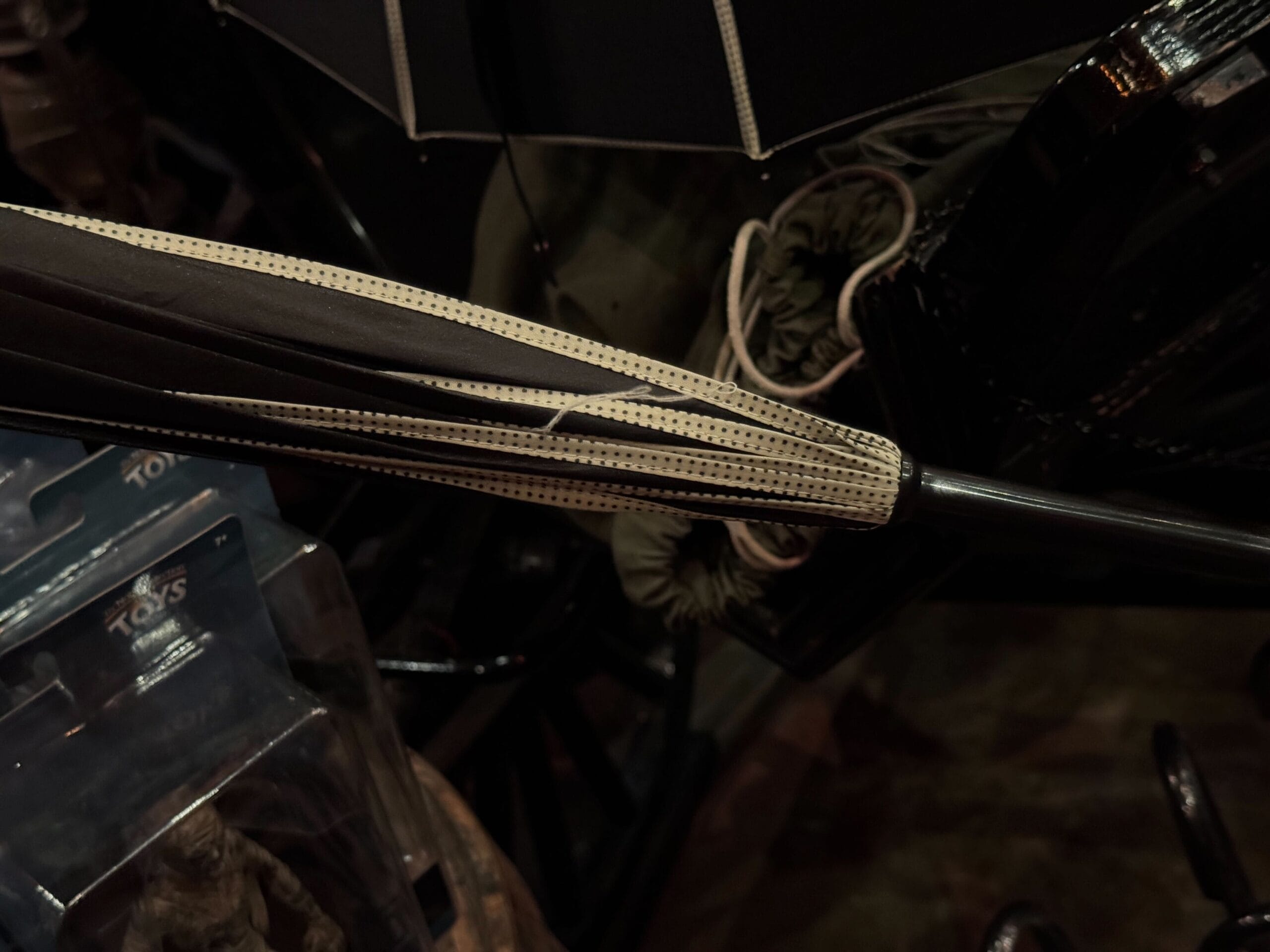 A closed black umbrella with a beige dotted edge, surrounded by dark objects and packaging.