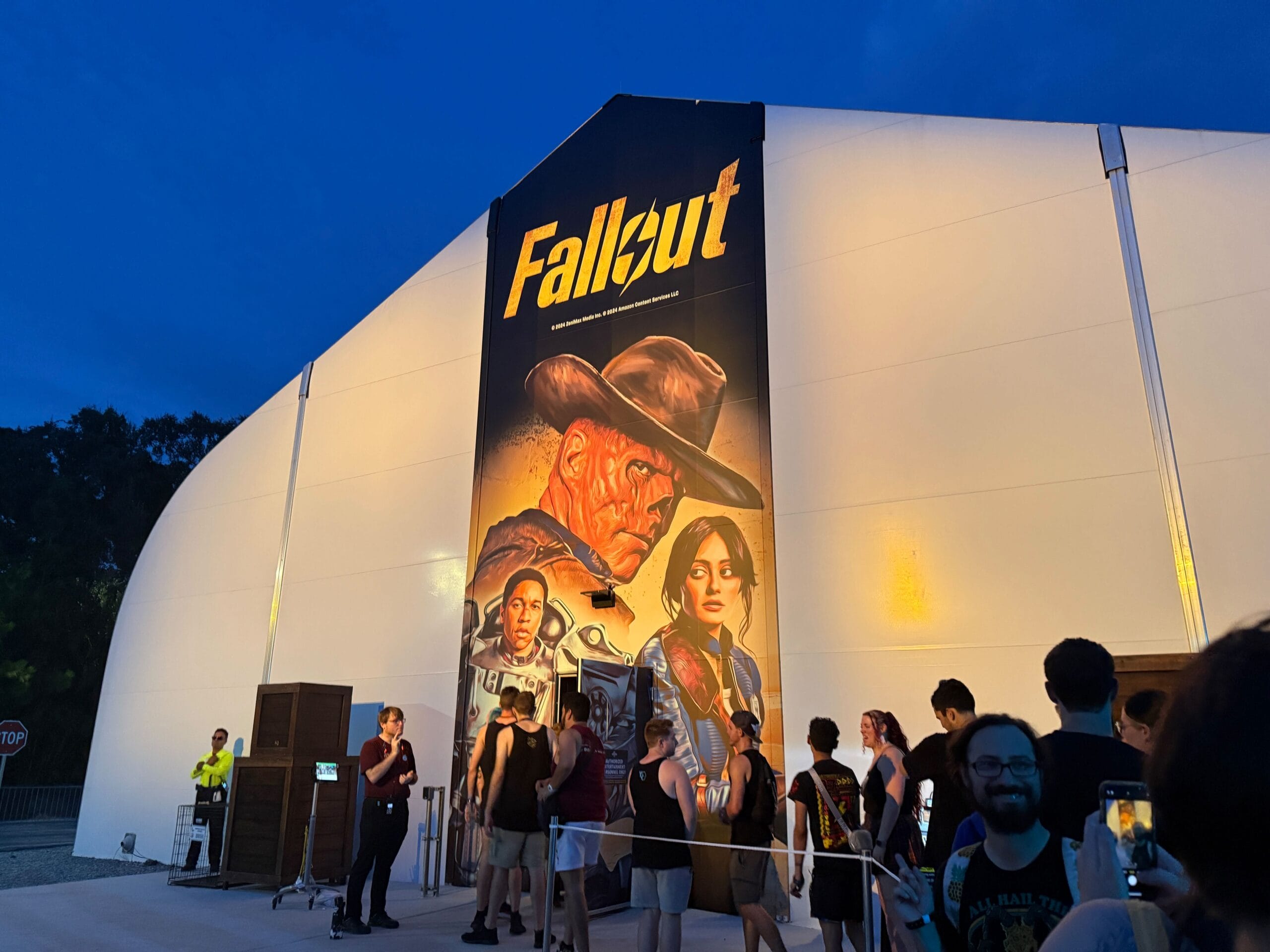 People line up outside a tent with a large Fallout poster for the House HHN 2025 event at dusk.