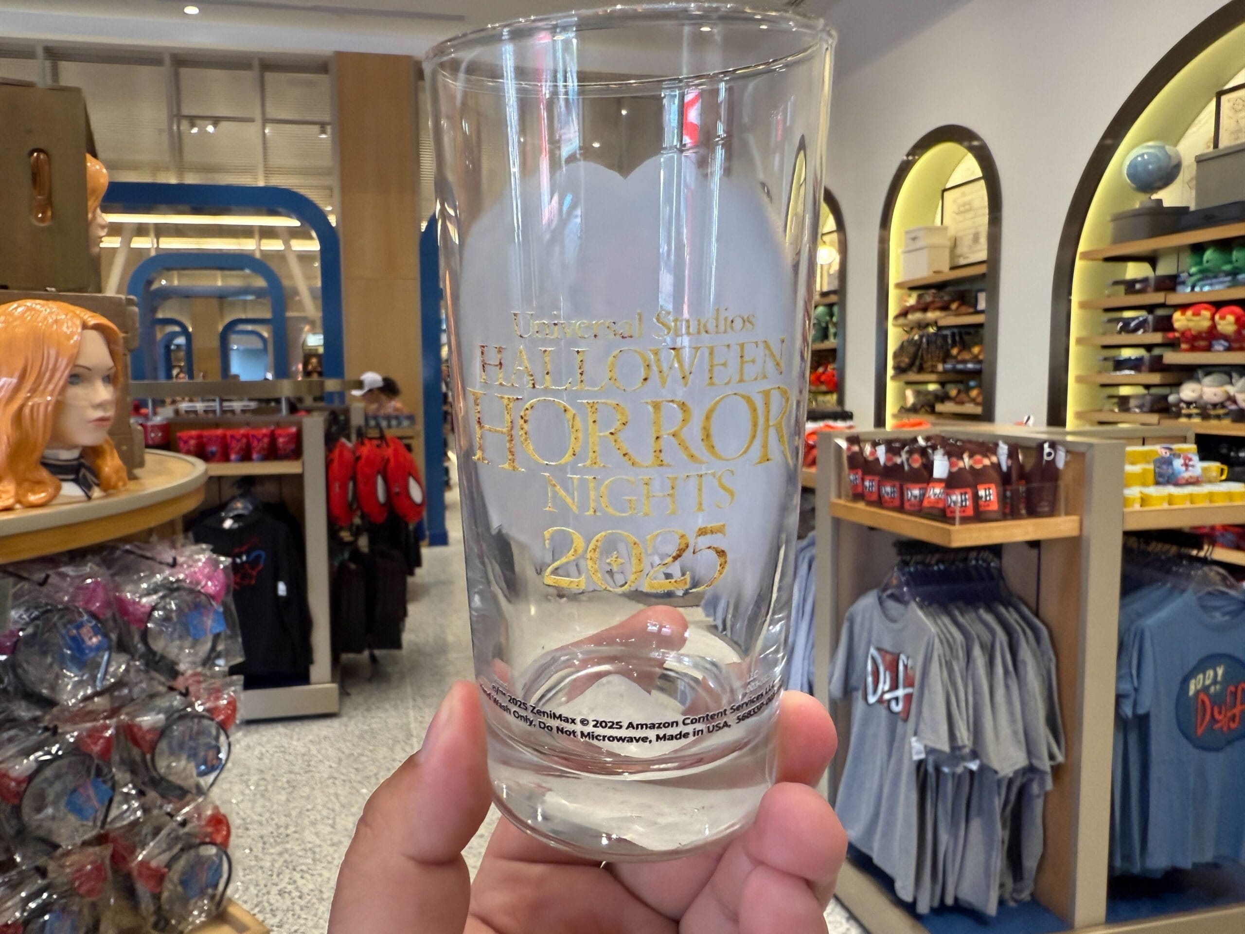 A hand holds a 2025 Halloween Horror Nights glass, showcasing HHN Merch 2025 at Universal Orlando Resort gift shop.