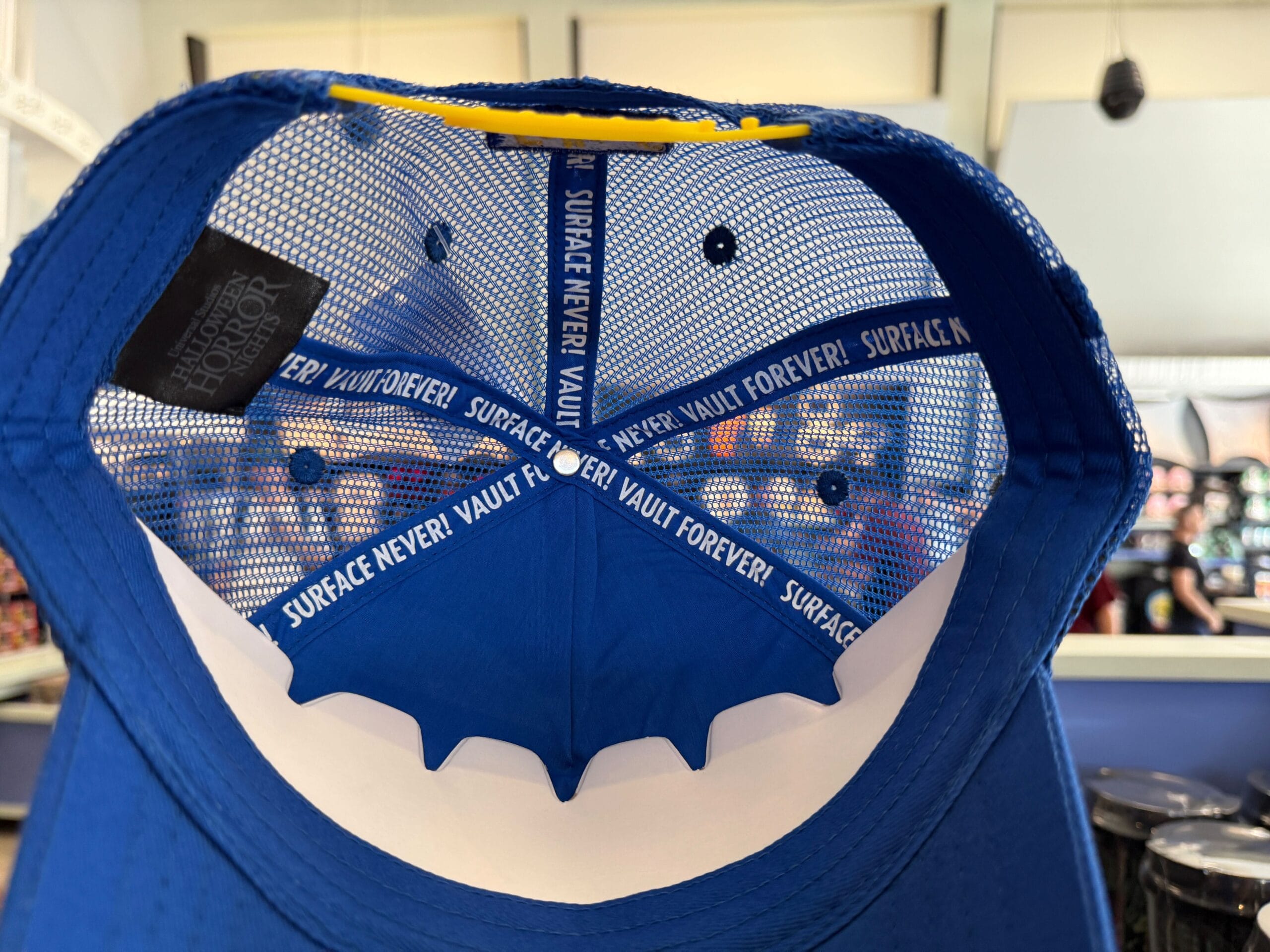 Inside view of a blue mesh cap, part of the HHN Merch 2025 at Universal Orlando Resort, with bold inner band text.