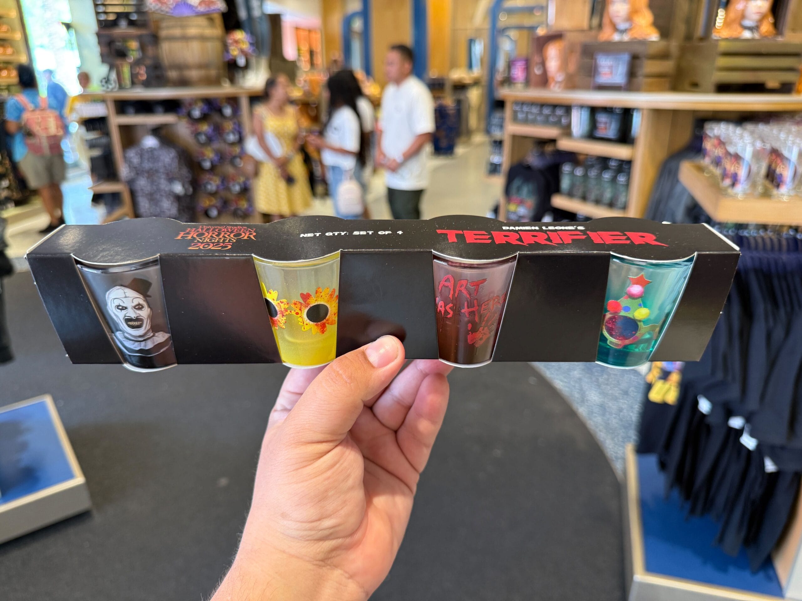 A hand holds a box of four "Terrifier" shot glasses, part of HHN Merch 2025 at Universal Orlando Resort.