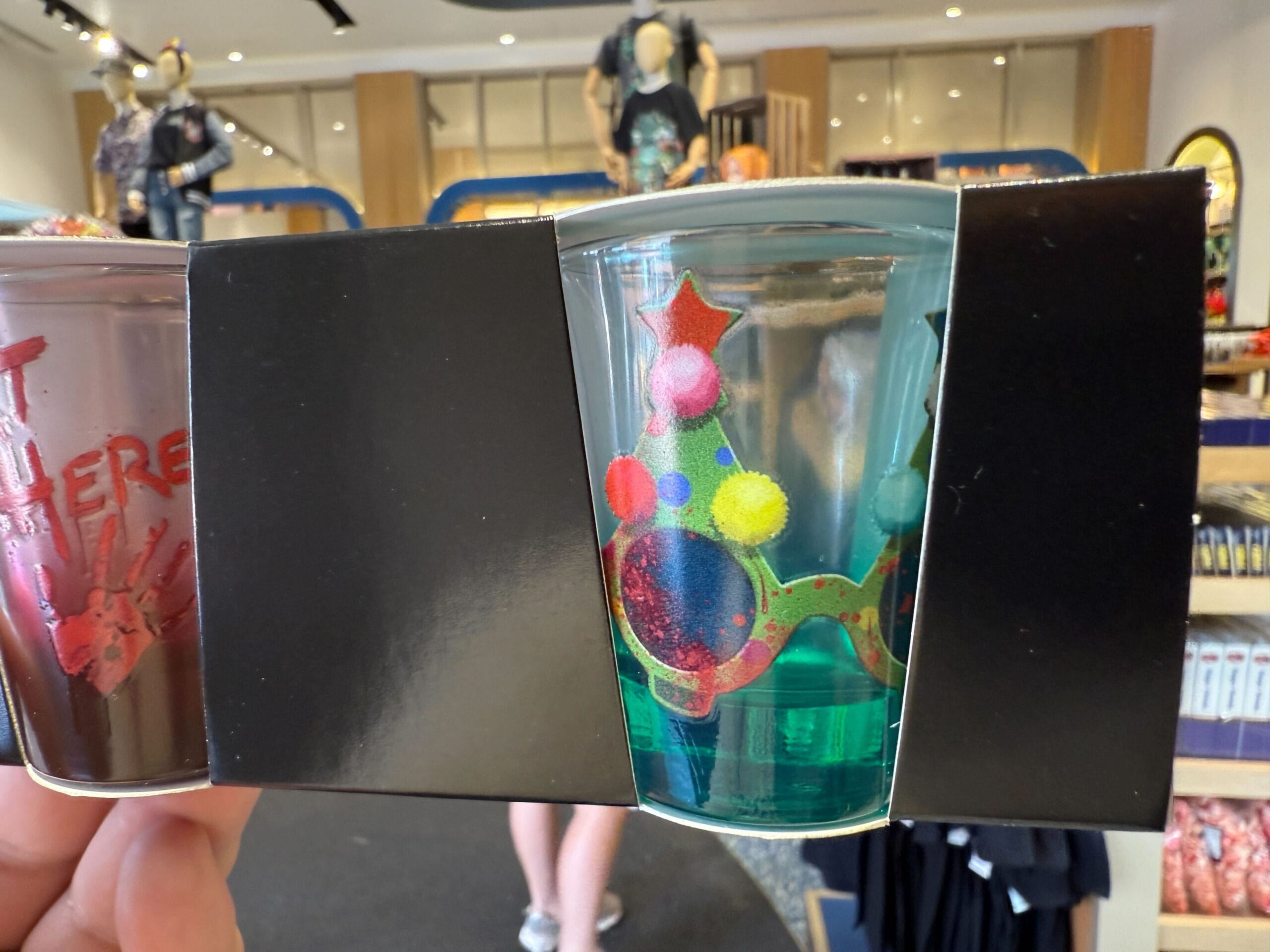 A glass with whimsical glasses design, held in a store amid shelves of Halloween Horror Nights Merchandise.