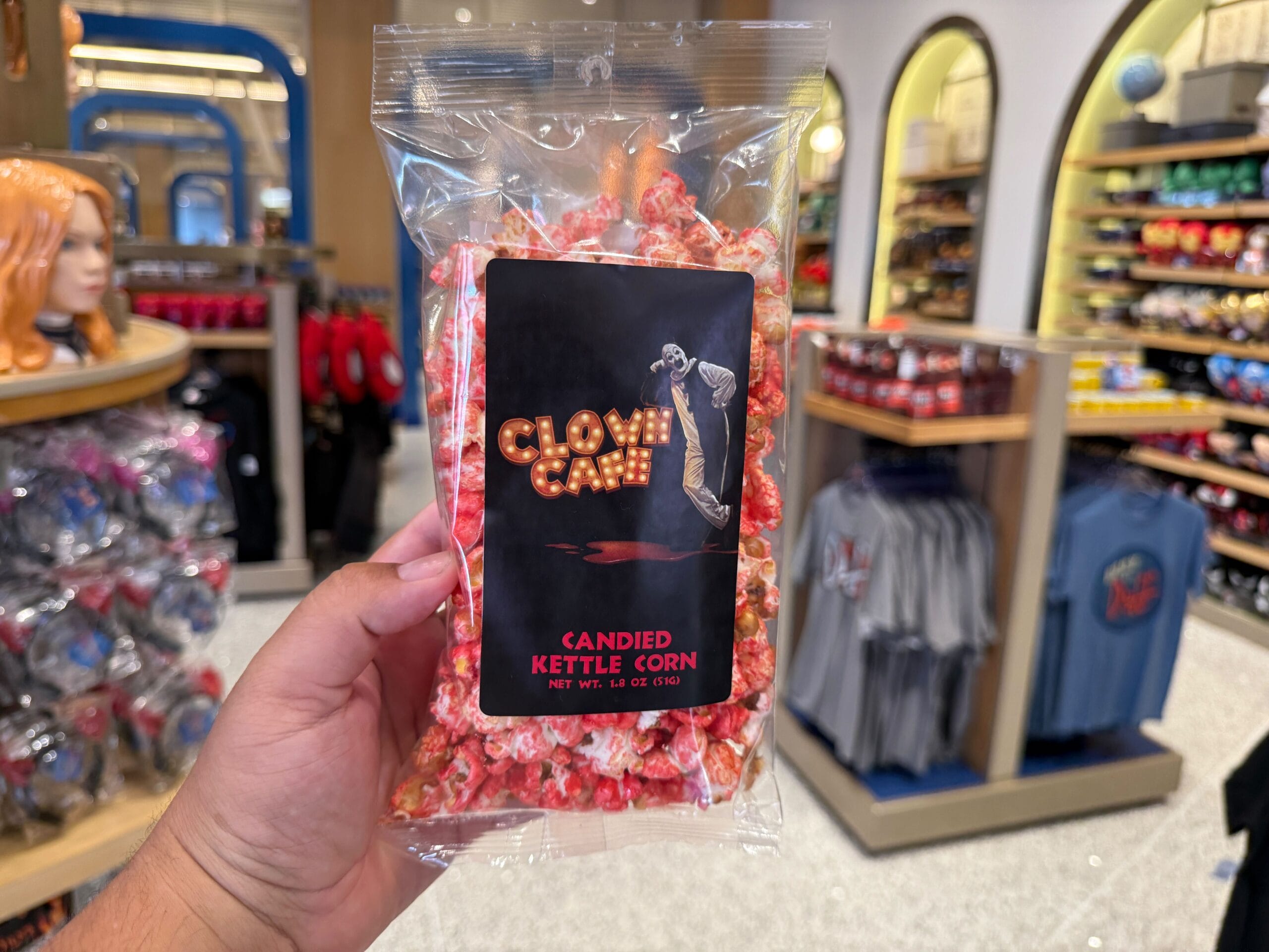 A hand holds Clown Café kettle corn amid Halloween Horror Nights Merchandise at Universal Orlando Resort.