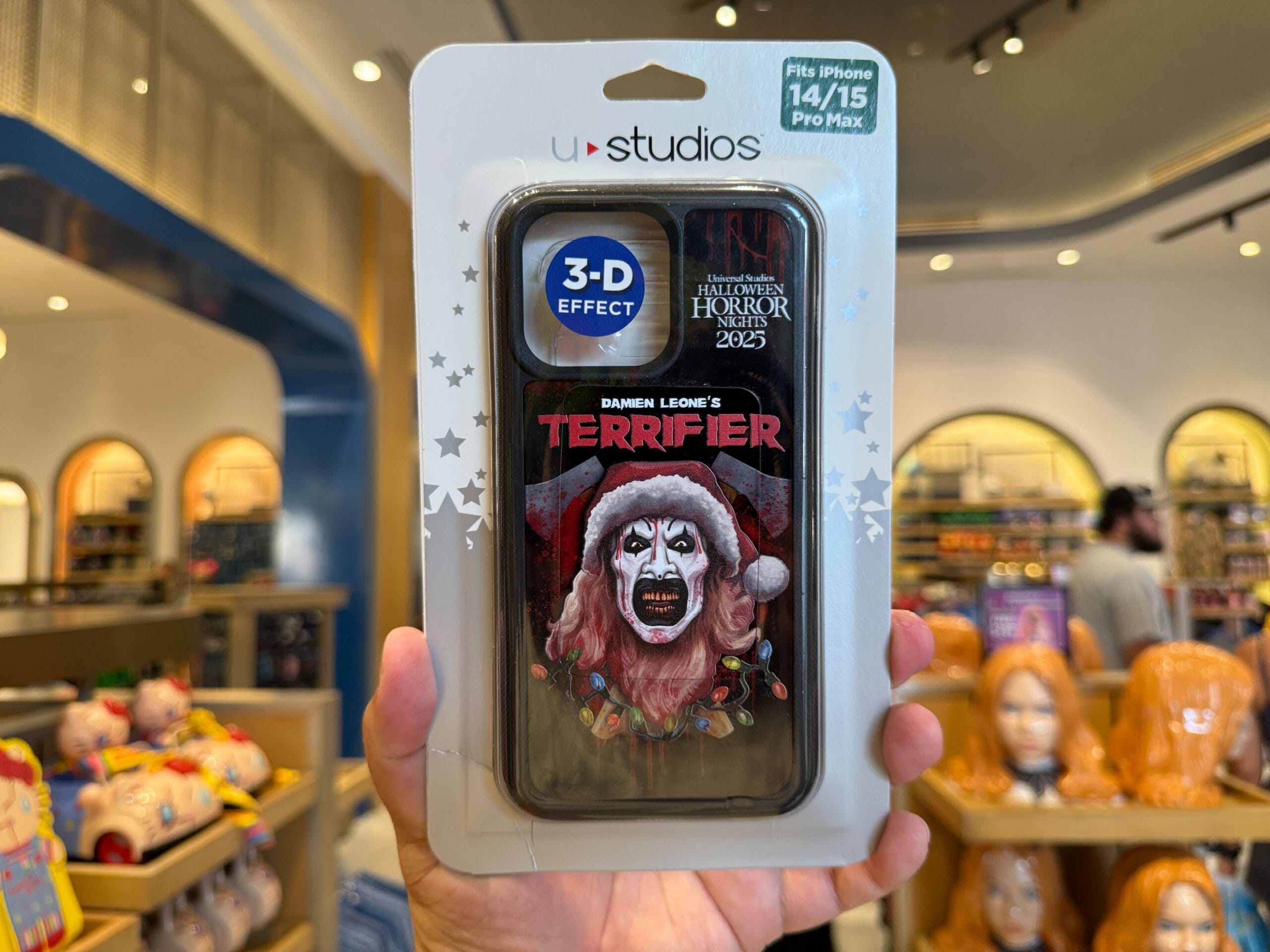 A hand holds a "Terrifier" 3-D phone case, scary clown in Santa hat, at a Halloween Horror Nights Merchandise store.