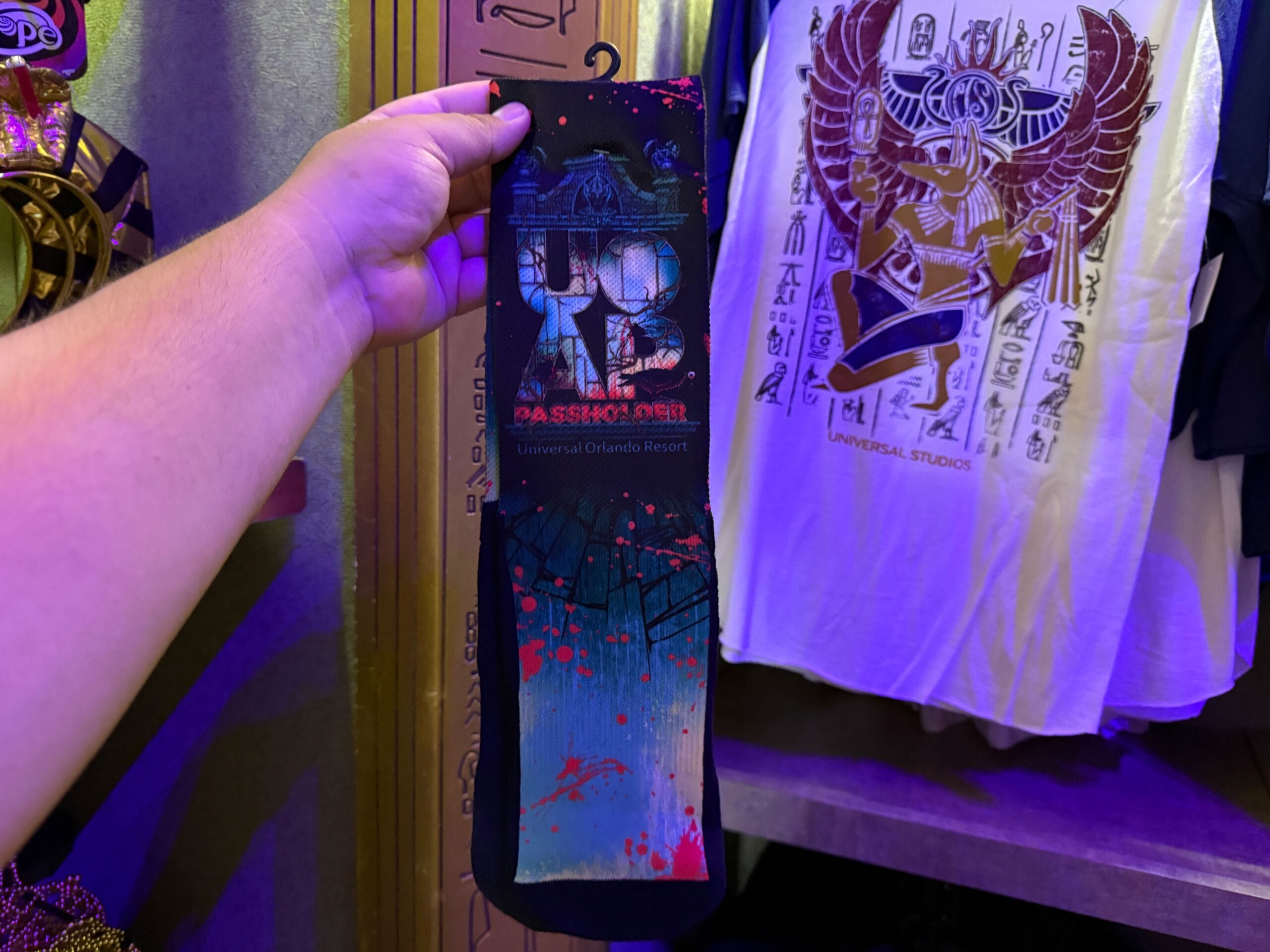 A hand holds a Universal Orlando Resort "UP ID Da Season Over" sock—spooky HHN Merch 2025 in a gift shop.