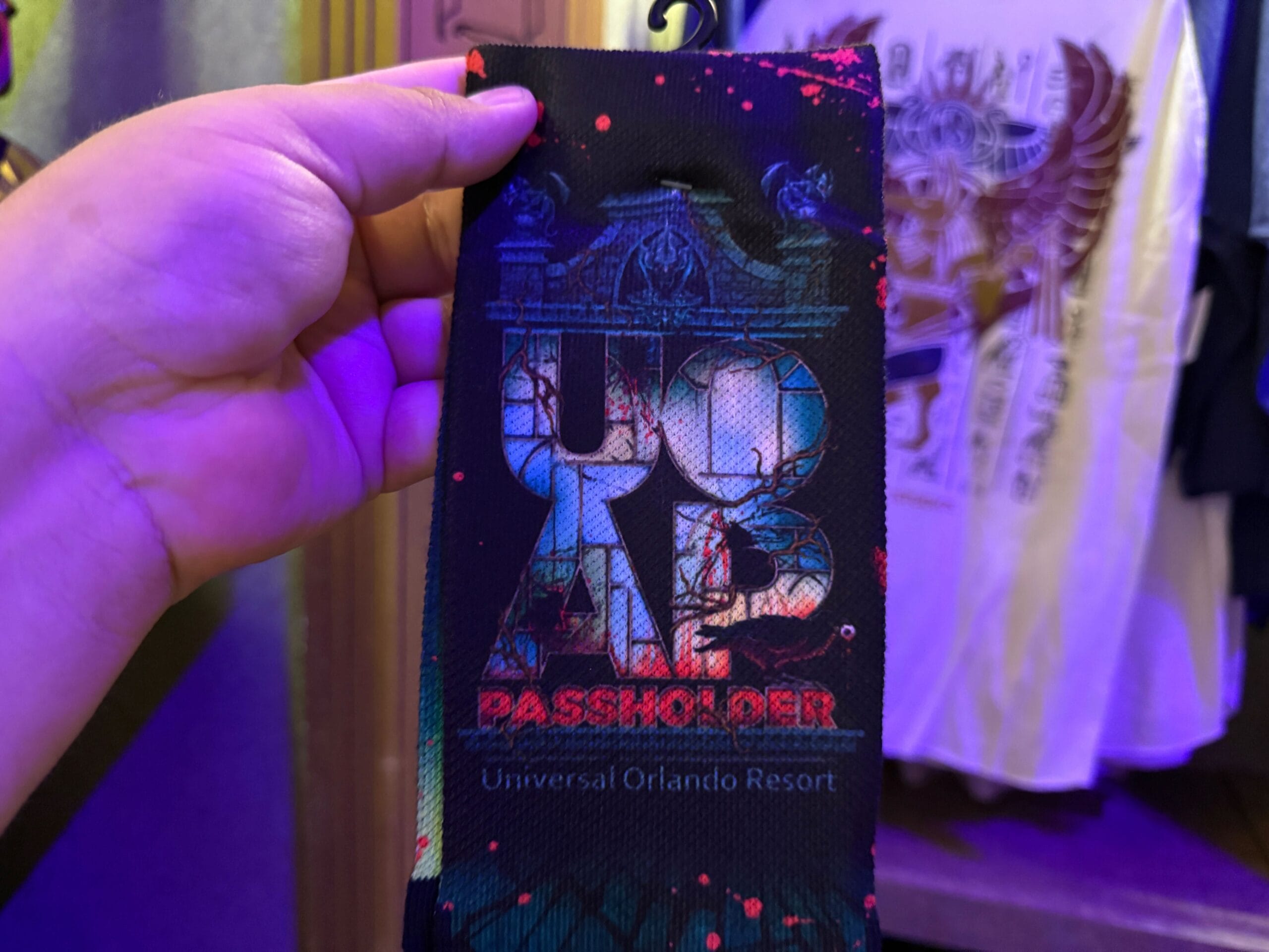 A hand holds a black Universal Orlando Resort Passholder ribbon, perfect for displaying your HHN Merch 2025.